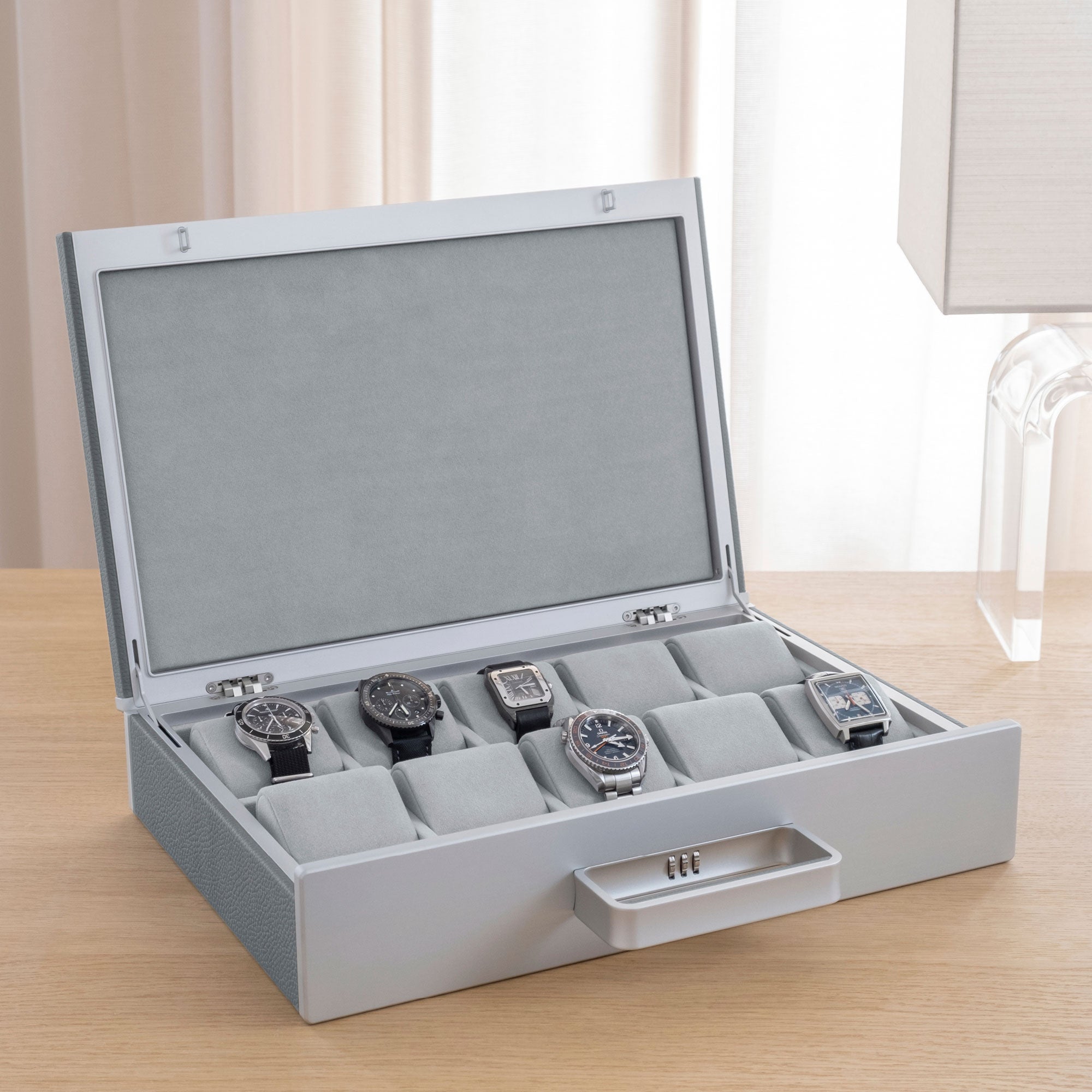 Lifestyle shot of open Mackenzie 10 Watch briefcase in carbon fiber and grey anodized aluminum casing, cloud grey leather and soft fog grey Alcantara made by hand filled with luxury watches including Jaeger-LeCoultre, Blancpain and Omega
