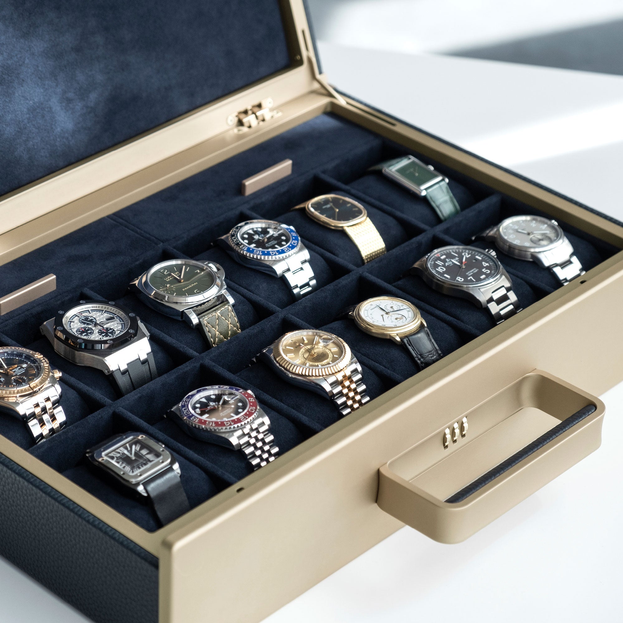 Lifestyle photo of Mackenzie Watch briefcase in gold anodized aluminum and carbon fiber and marine leather holding a collection of luxury watches, including Audemars Piguet, Patek Philippe, Rolex, Alpina and Cartier. 