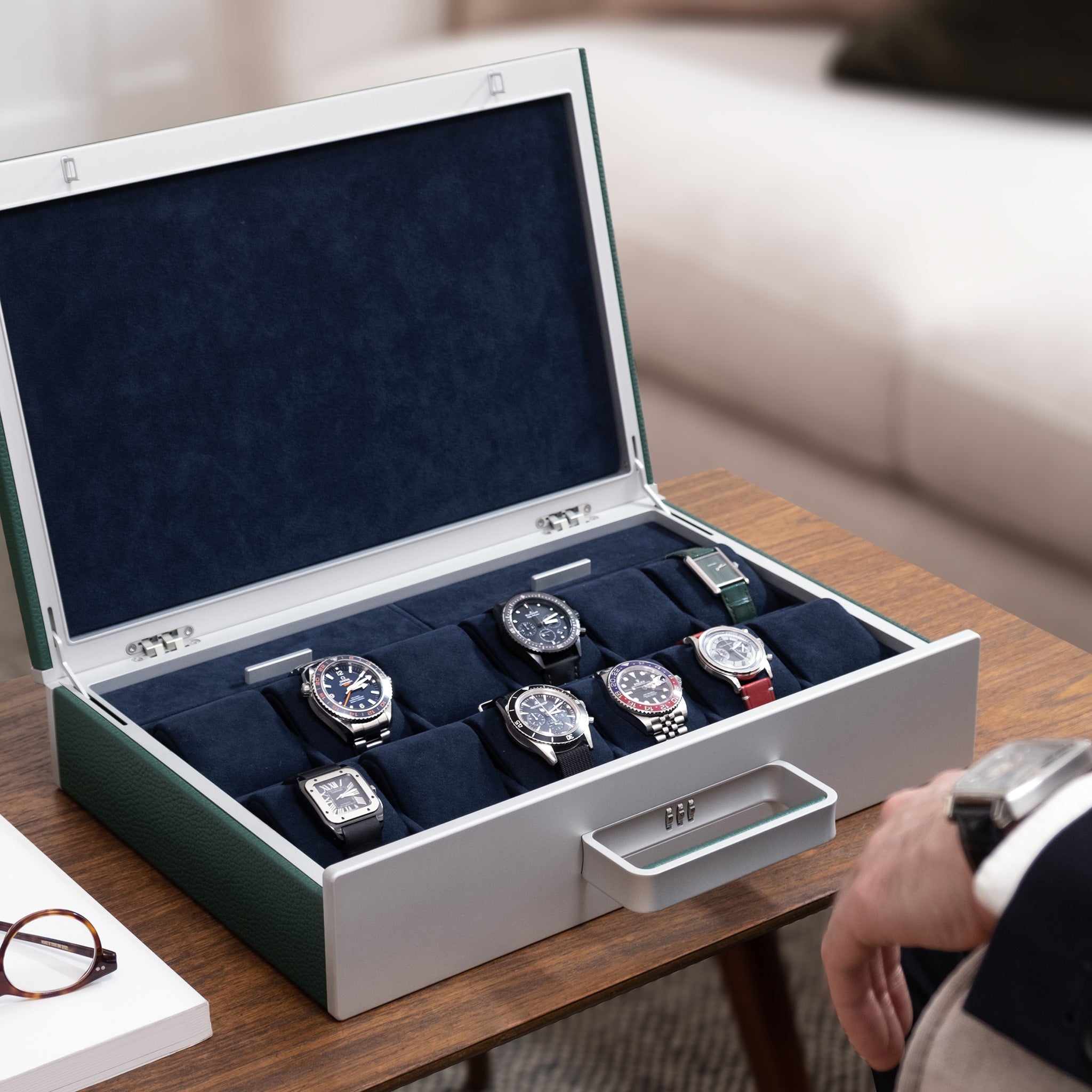 Lifestyle shot of open Mackenzie 12 Watch briefcase in carbon fiber and grey anodized aluminum casing, emerald leather and soft deep blue Alcantara made by hand filled with luxury watches including Rolex, Jaeger-LeCoultre, Blancpain and Omega