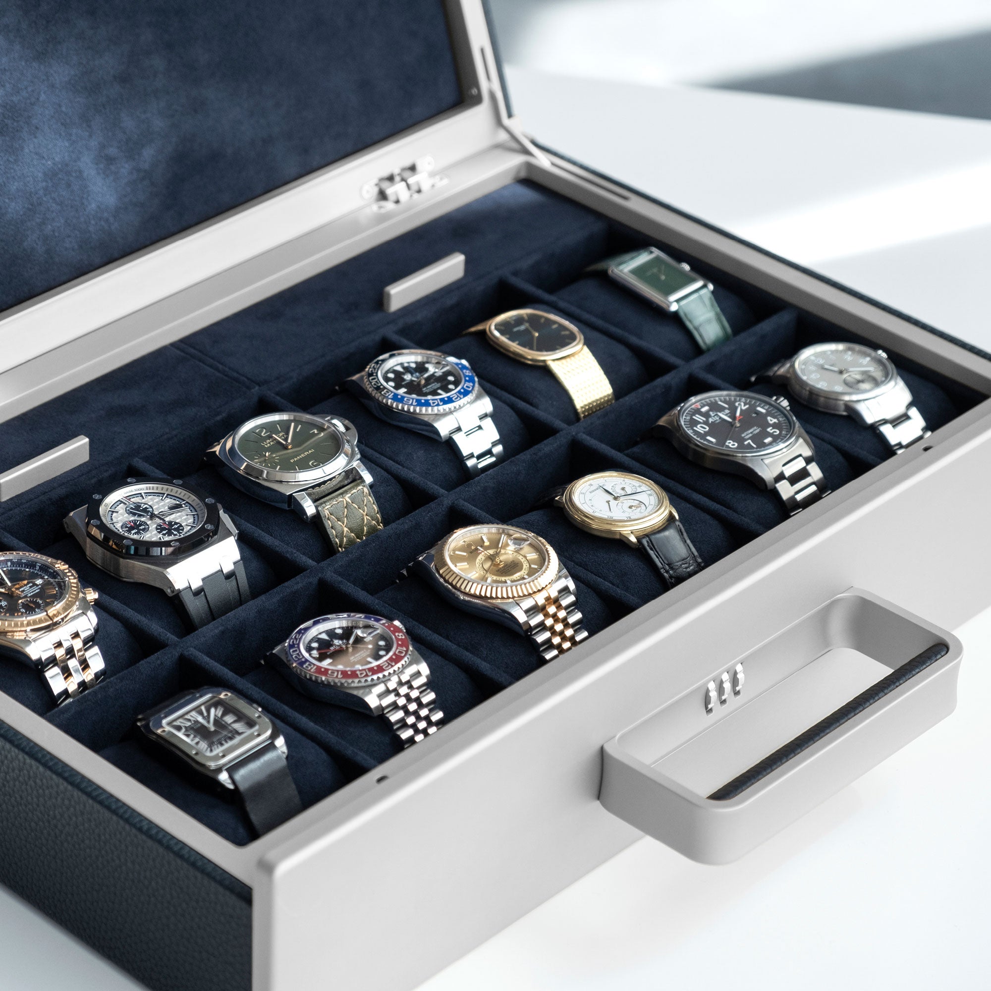 Lifestyle photo of Charles Simon x Paris Watch Club Mackenzie Watch briefcase in grey anodized aluminum and carbon fiber and marine leather holding a collection of luxury watches, including Audemars Piguet, Patek Philippe, Rolex, Alpina and Cartier. 