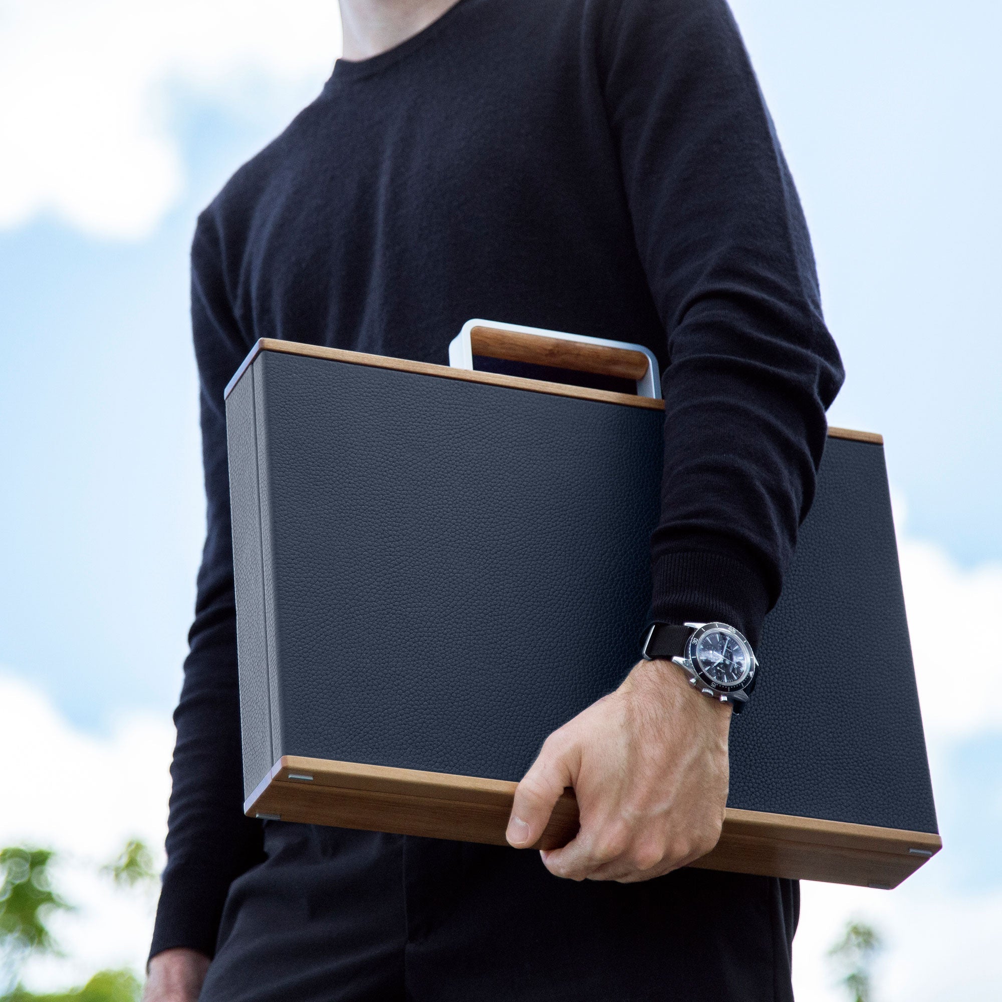 Lifestyle shot of sustainable watch briefcase made from recycled wood, fine French leather and carbon fiber and anodized aluminum casing being held by man wearing luxury watch
