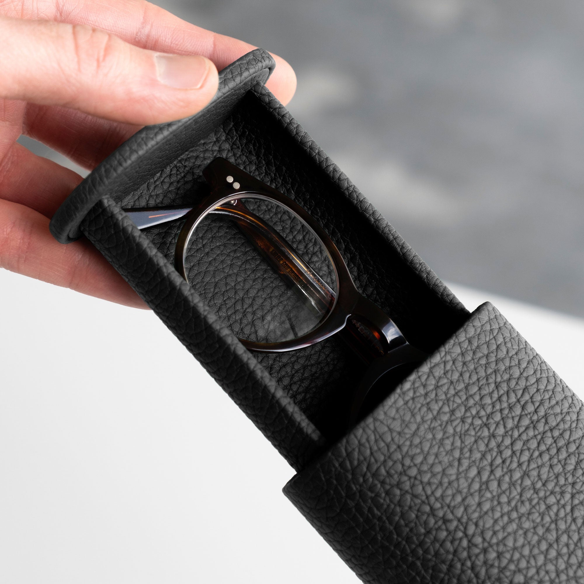 Man opening his black leather watch roll containing a pair of glasses