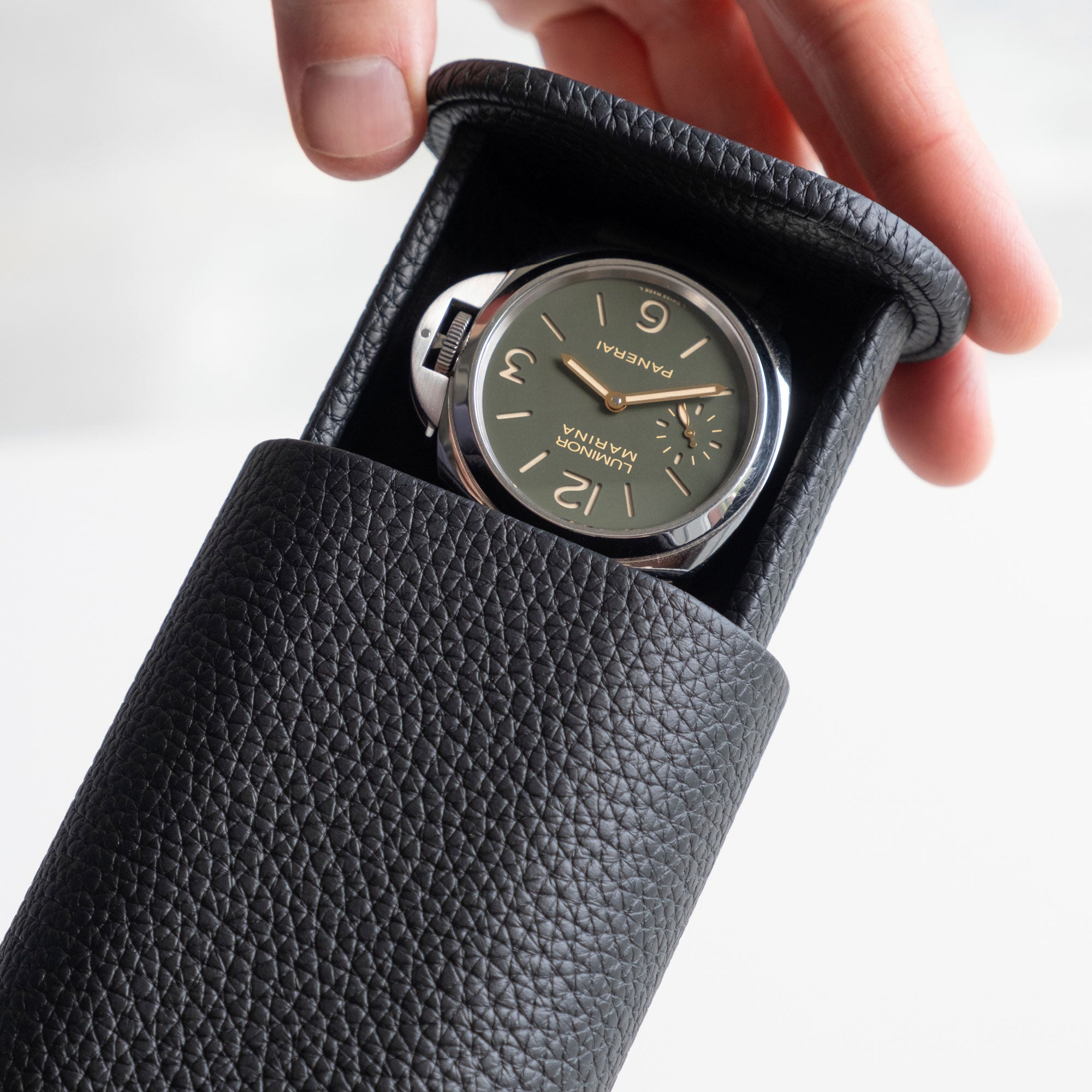 Detail photo of man opening the Oscar Tall Leather Watch roll in black to reveal a Panerai watch held inside.