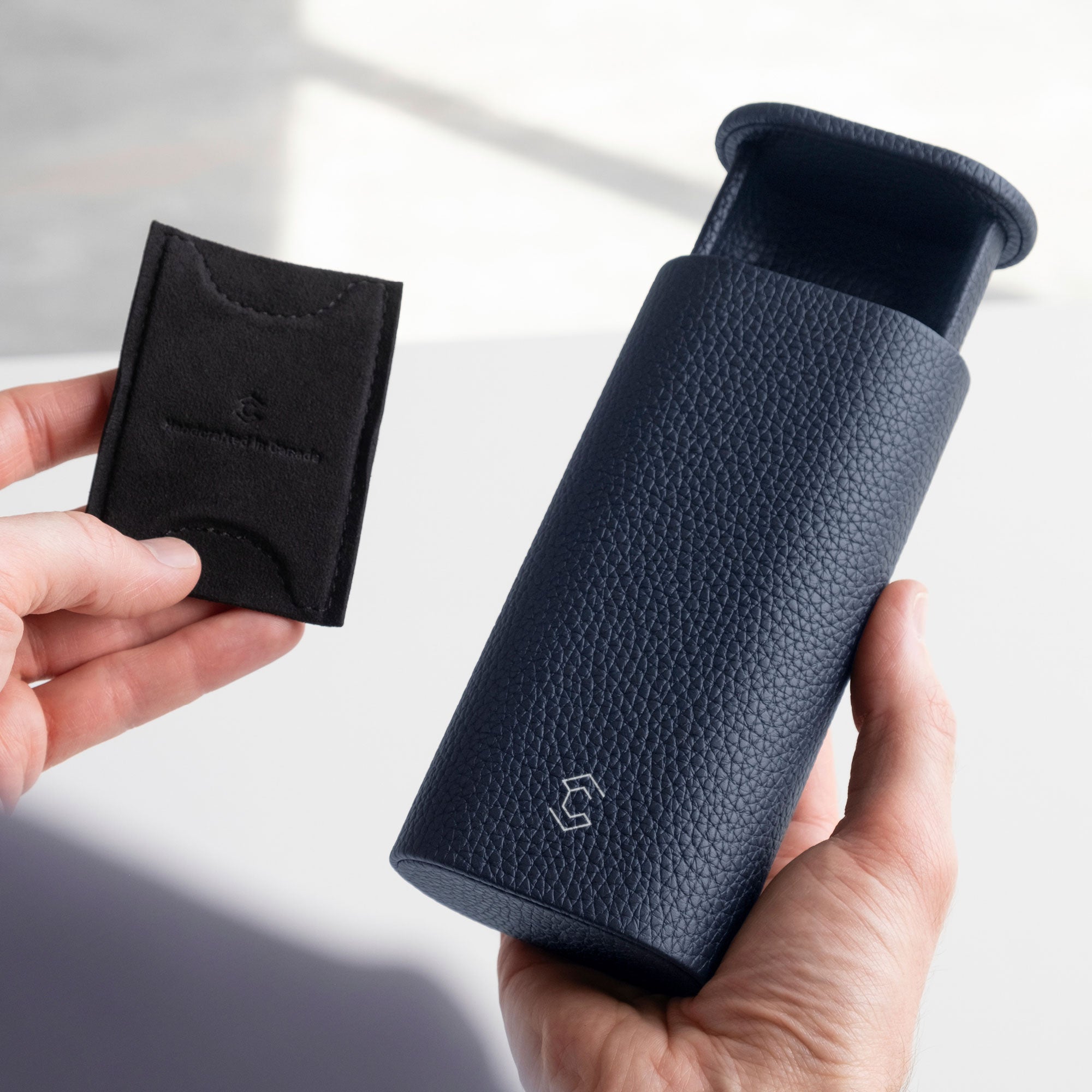 Man holding open marine Oscar leather watch roll in one hand and removable card inserts in different sizes to keep the watch in place in the other hand.