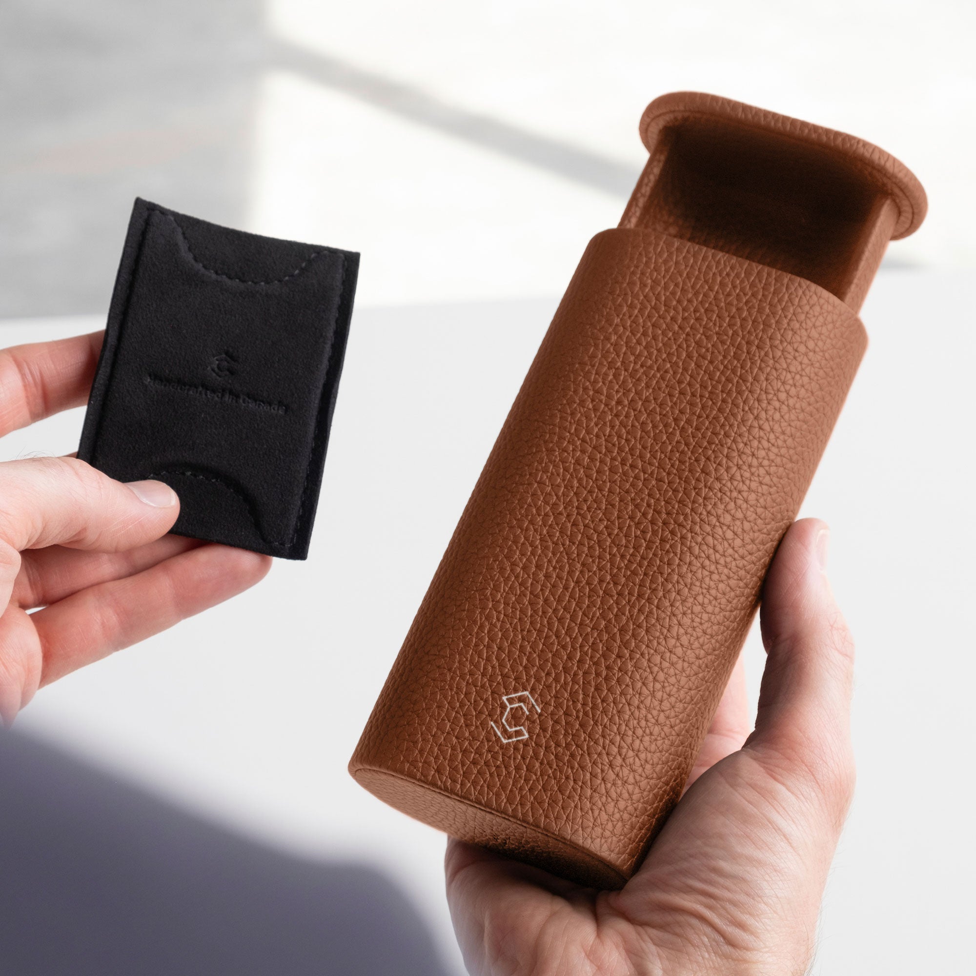 Man holding open tan leather Oscar leather watch roll in one hand and removable card insert to keep the watch in place in the other hand. 