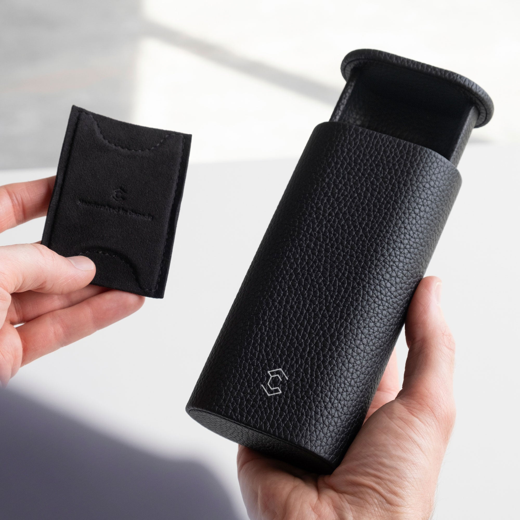 Man holding open black leather Oscar travel watch roll in one hand and removable card insert to keep the watch in place in the other hand. 