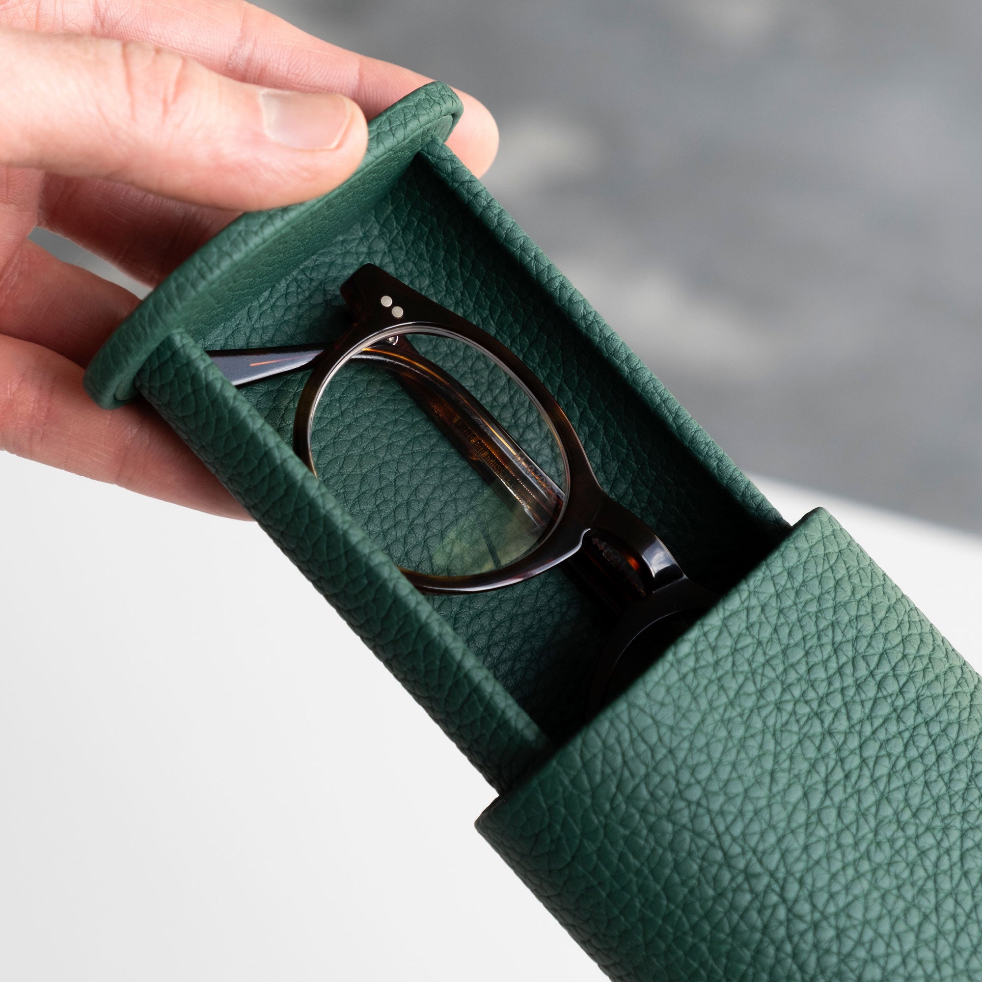 Man sliding open his emerald leather Oscar 1 Tall Watch roll which holds a pair of glasses