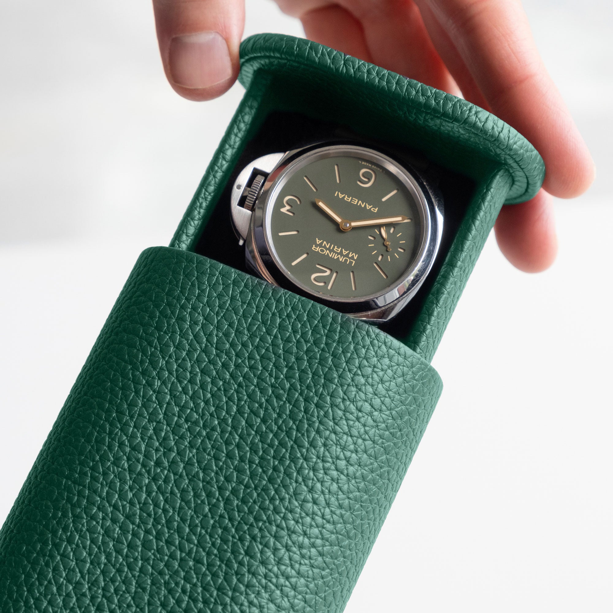 Detail photo of man opening the emerald leather Oscar Tall Watch roll holding a Panerai men's luxury watch