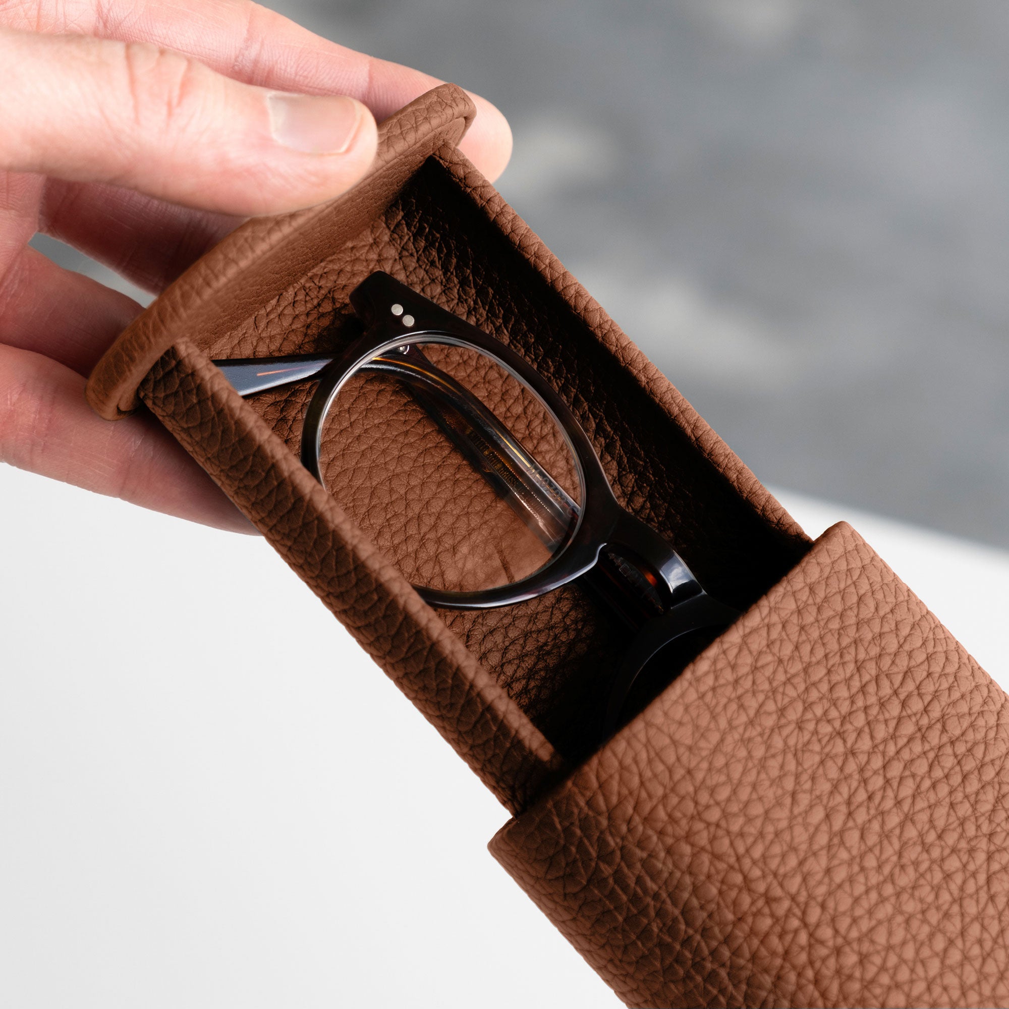 Man opening his tan leather Oscar Tall Watch roll containing a pair of glasses