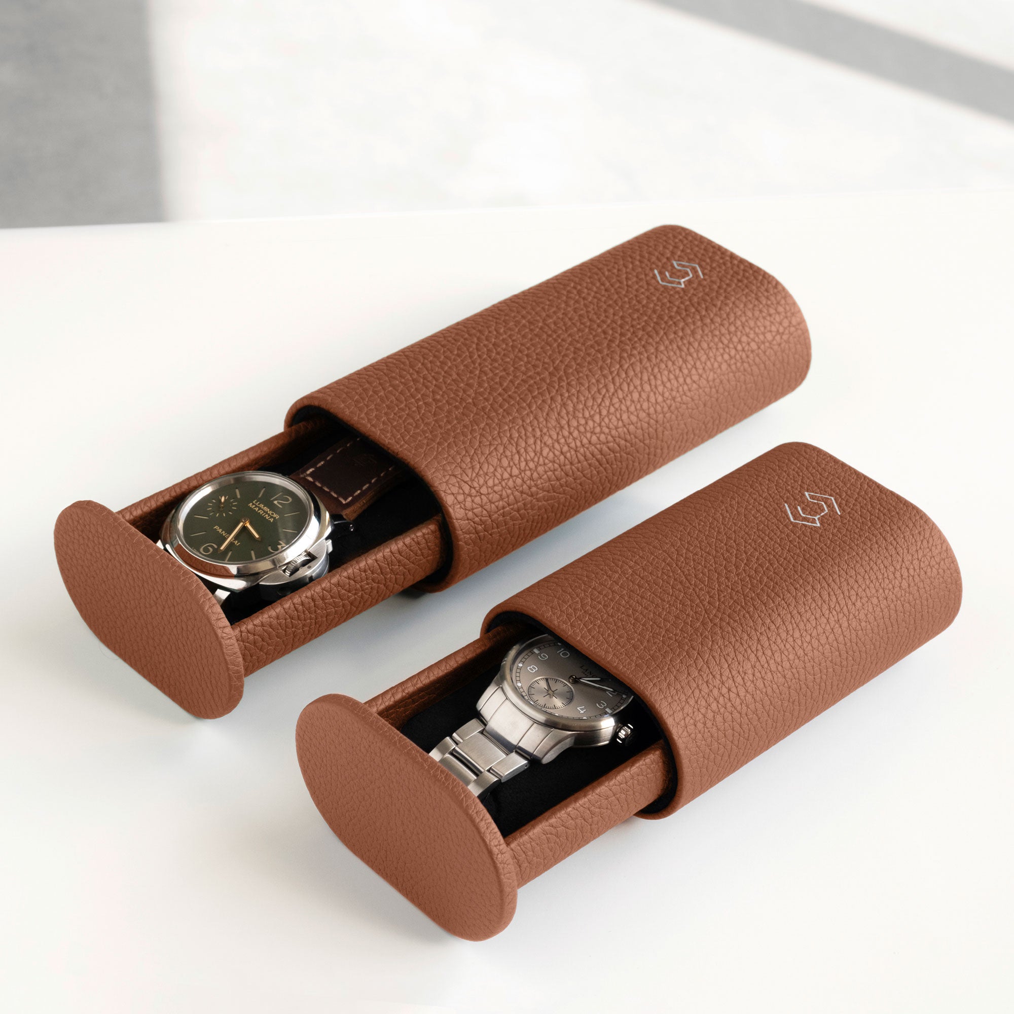 Lifestyle photo of two leather watch rolls in tan. The Oscar 1 Tall for watches with a watch strap on the left and the Oscar 1 for watches with a metal bracelet on the right