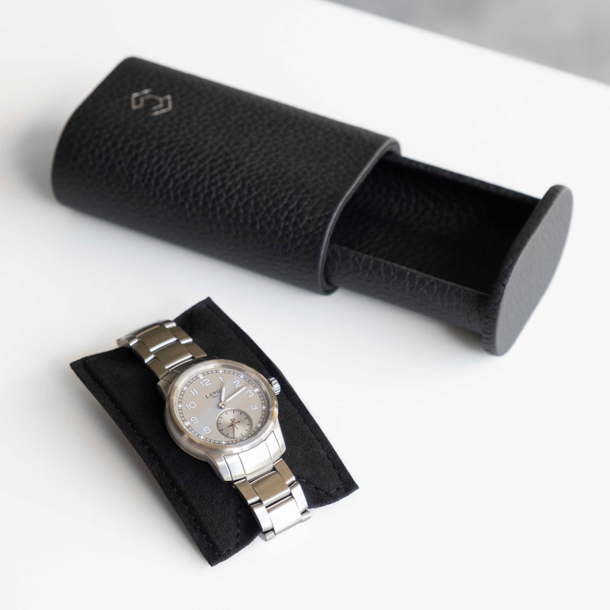 Lifestyle photo of open black leather watch roll with men's watch with metal bracelet placed on card insert that keeps luxury watch firmly in place
