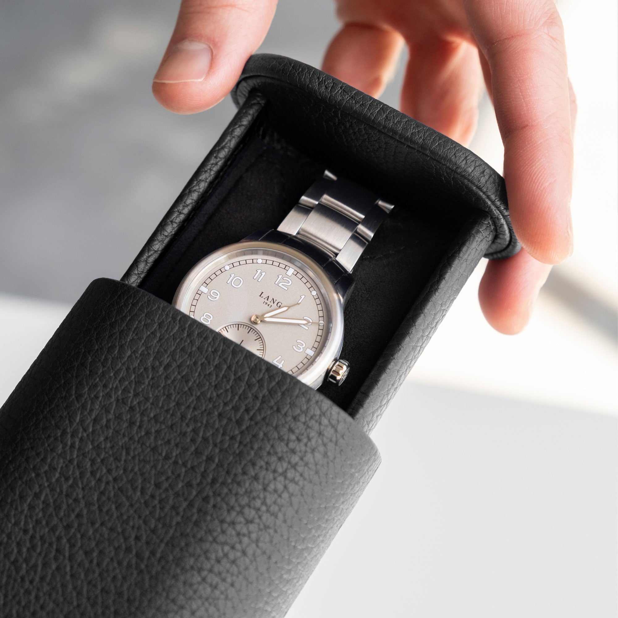 Detail photo of man opening his black leather watch roll by Charles Simon that holds one watch with a metal bracelet