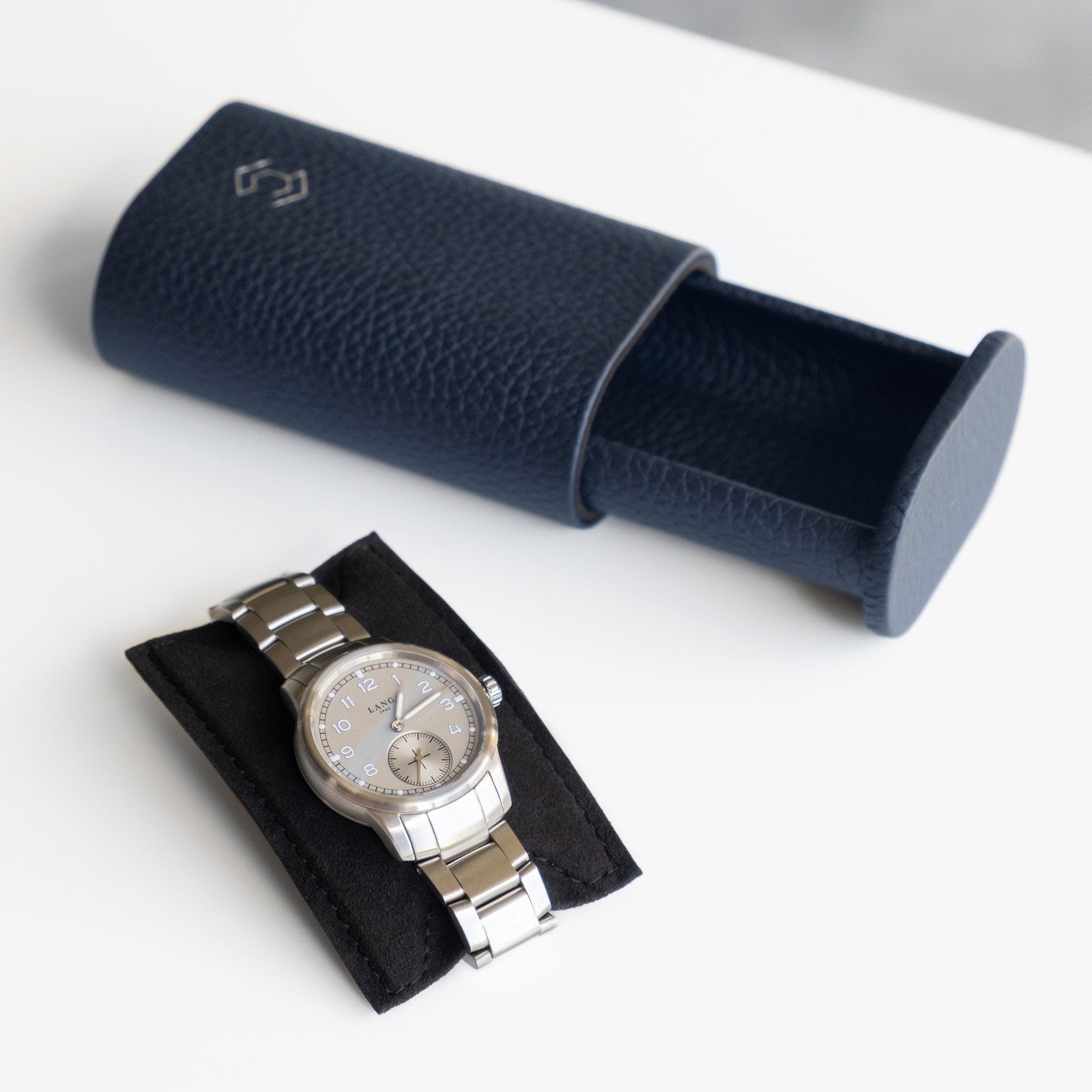 Lifestyle photo of open marine Taurillon leather watch roll with men's watch with metal bracelet placed on card insert to keep the watch firmly in place