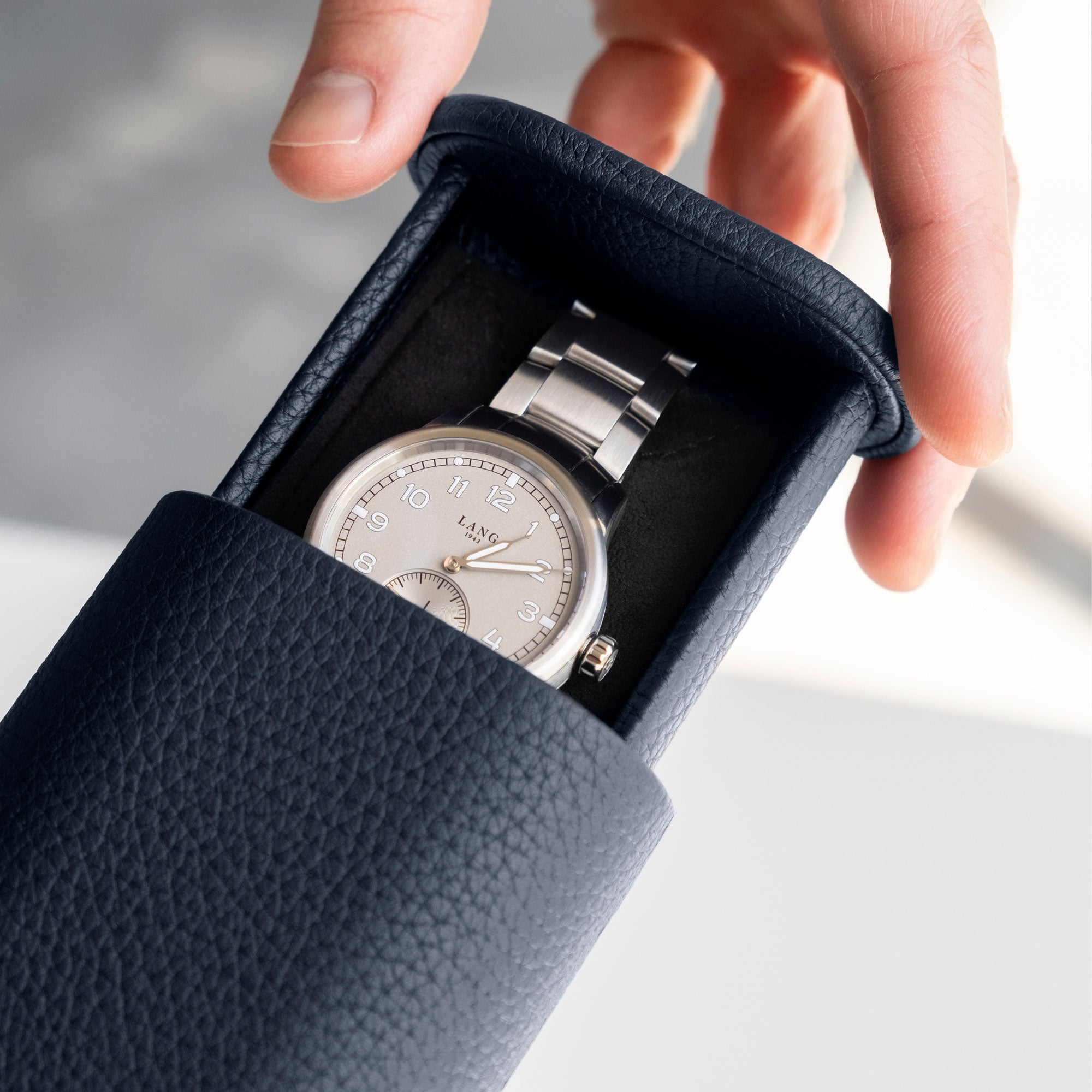  Closeup detail photo of man opening his marine french leather Oscar 1 Watch roll that holds one watch with a metal bracelet