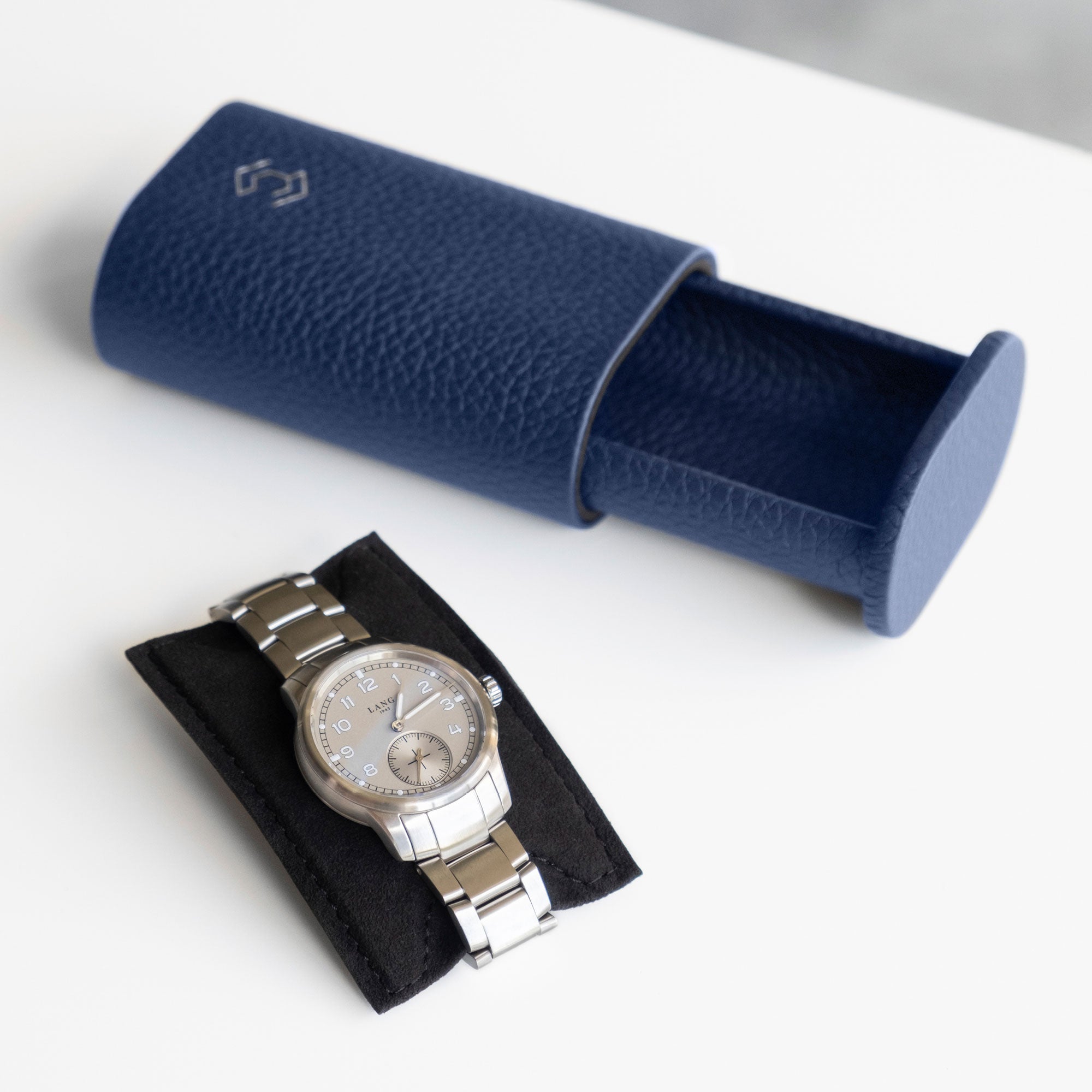 Men's watch placed on removable card insert made from black Alcantara to hold the watch in place. An open sapphire leather Oscar 1 Watch roll is placed in the background.