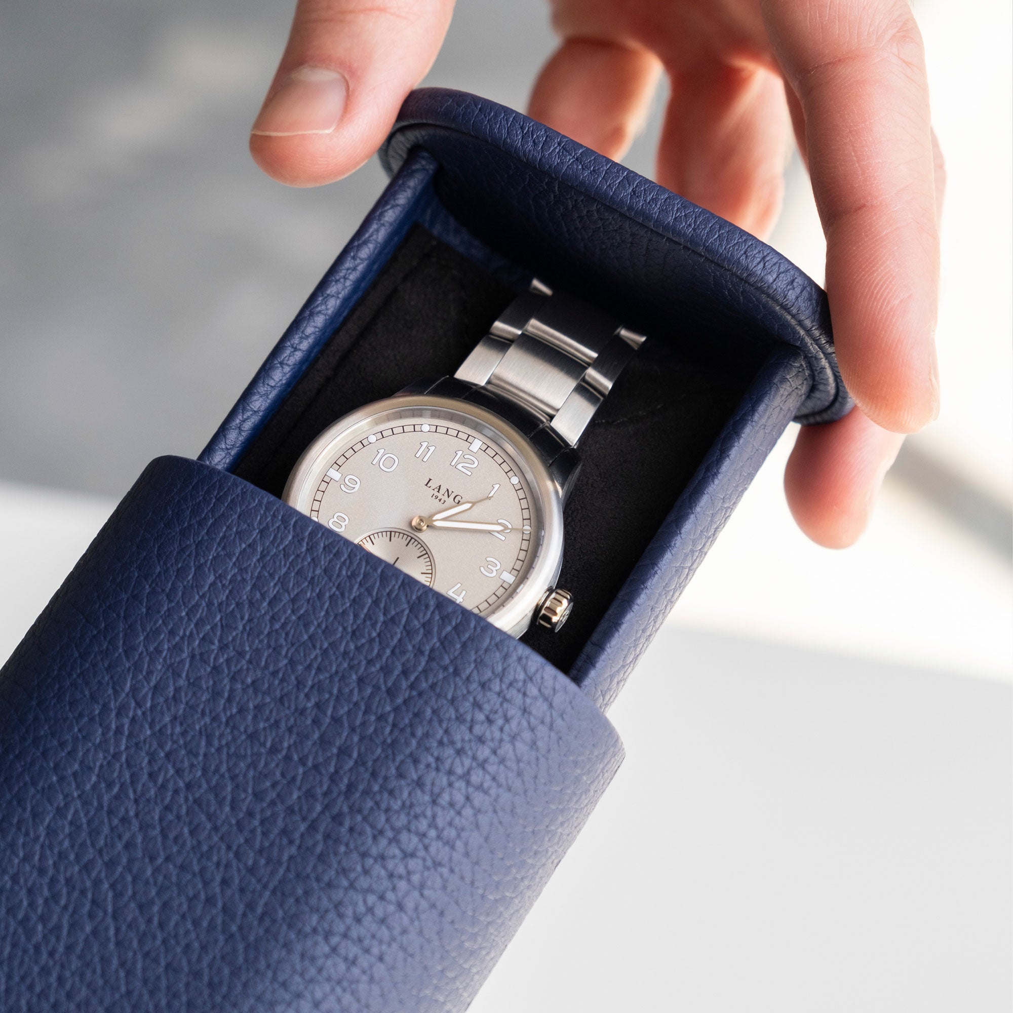 Detail photo of man opening his sapphire leather Oscar 1 Watch roll with a luxurious men's watch placed inside of it.