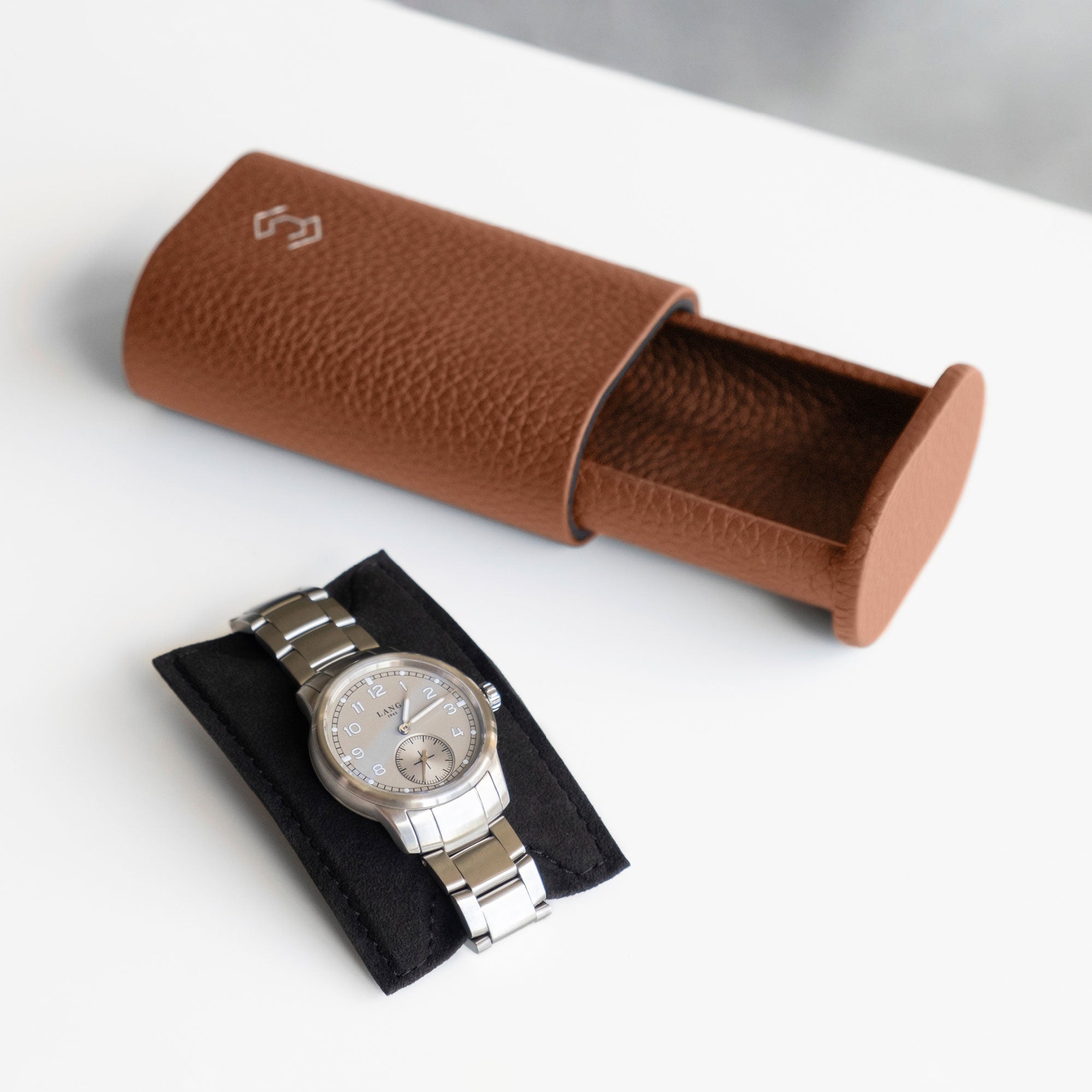 Lifestyle photo of open tan leather watch roll with men’s watch with metal bracelet placed on card insert that keeps luxury watch firmly in place