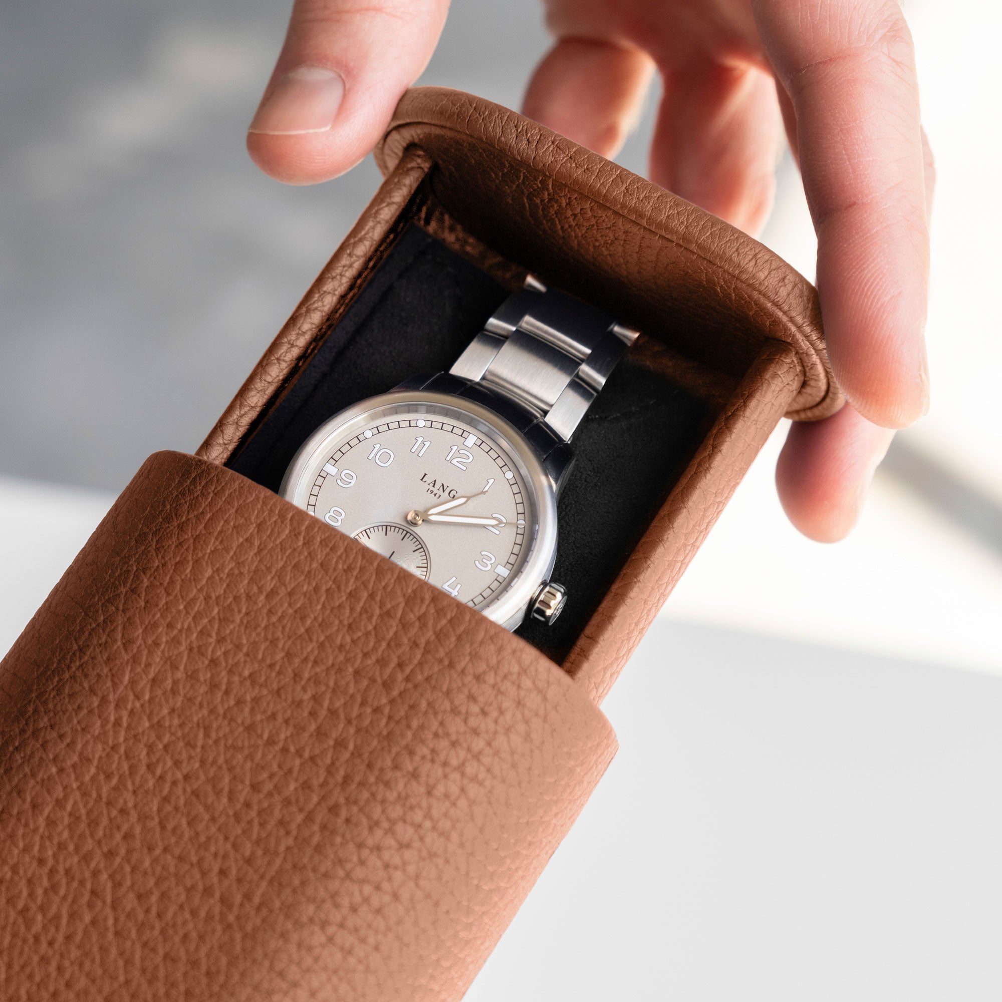 Detail photo of man opening his tan leather Oscar 1 Watch roll that holds one watch with a metal bracelet