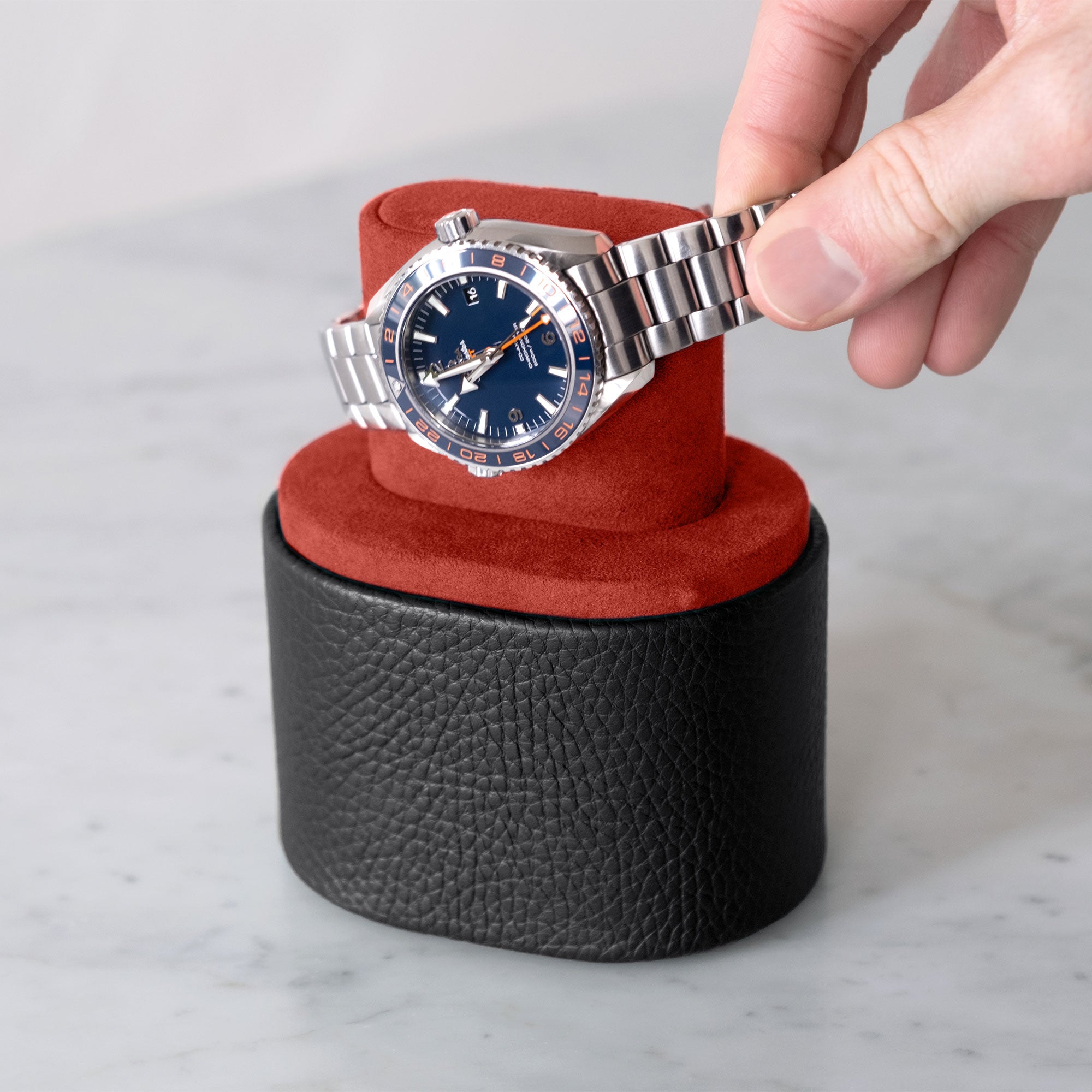 Lifestyle shot of man taking  Omega Seamaster Planet Ocean 600M Good Planet luxury watch from designer Theo travel watch roll in black leather and Vermilion Alcantara watch cushion