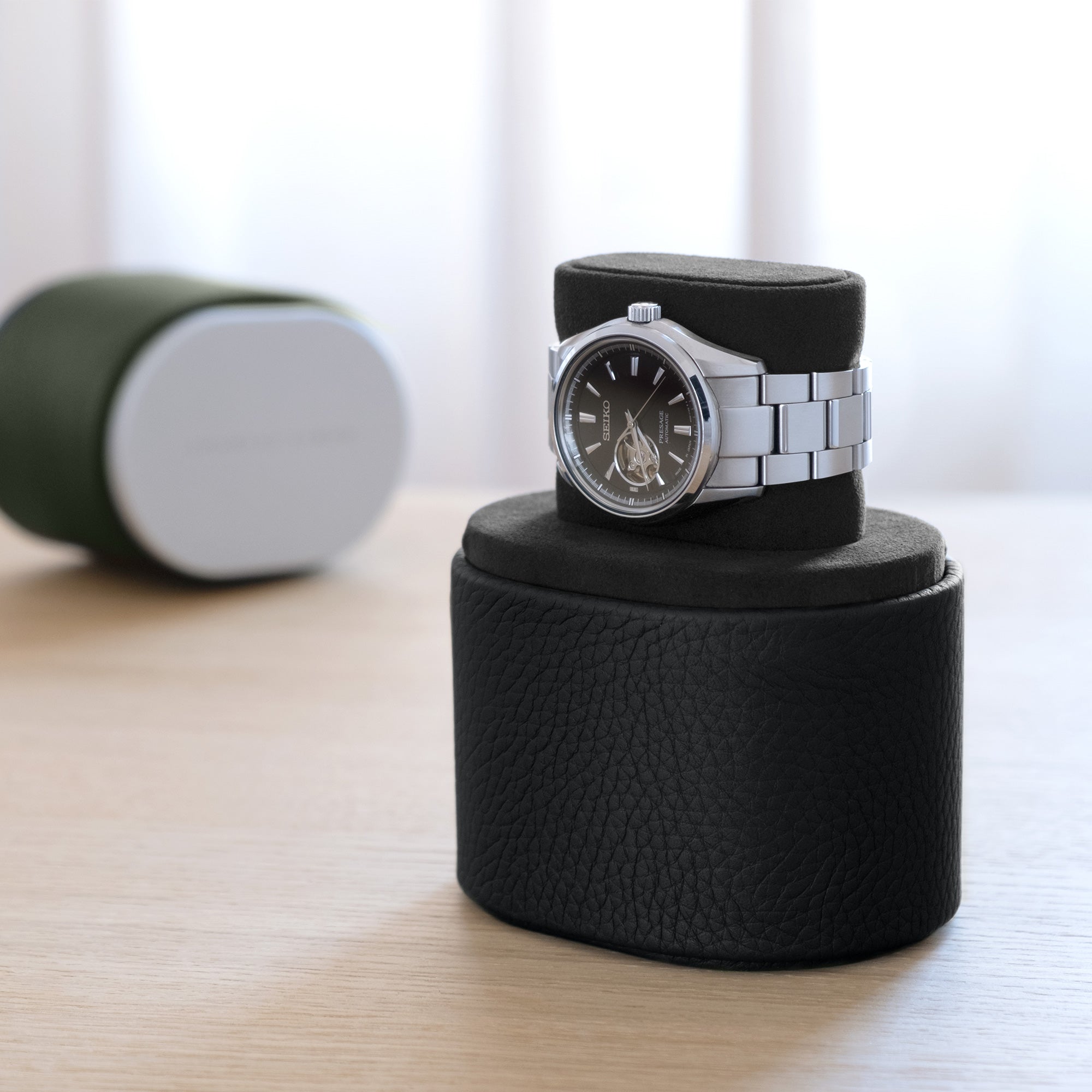 Lifestyle shot of all black Theo watch roll in convenient portable watch stand position with closed khaki Theo single watch roll in the background