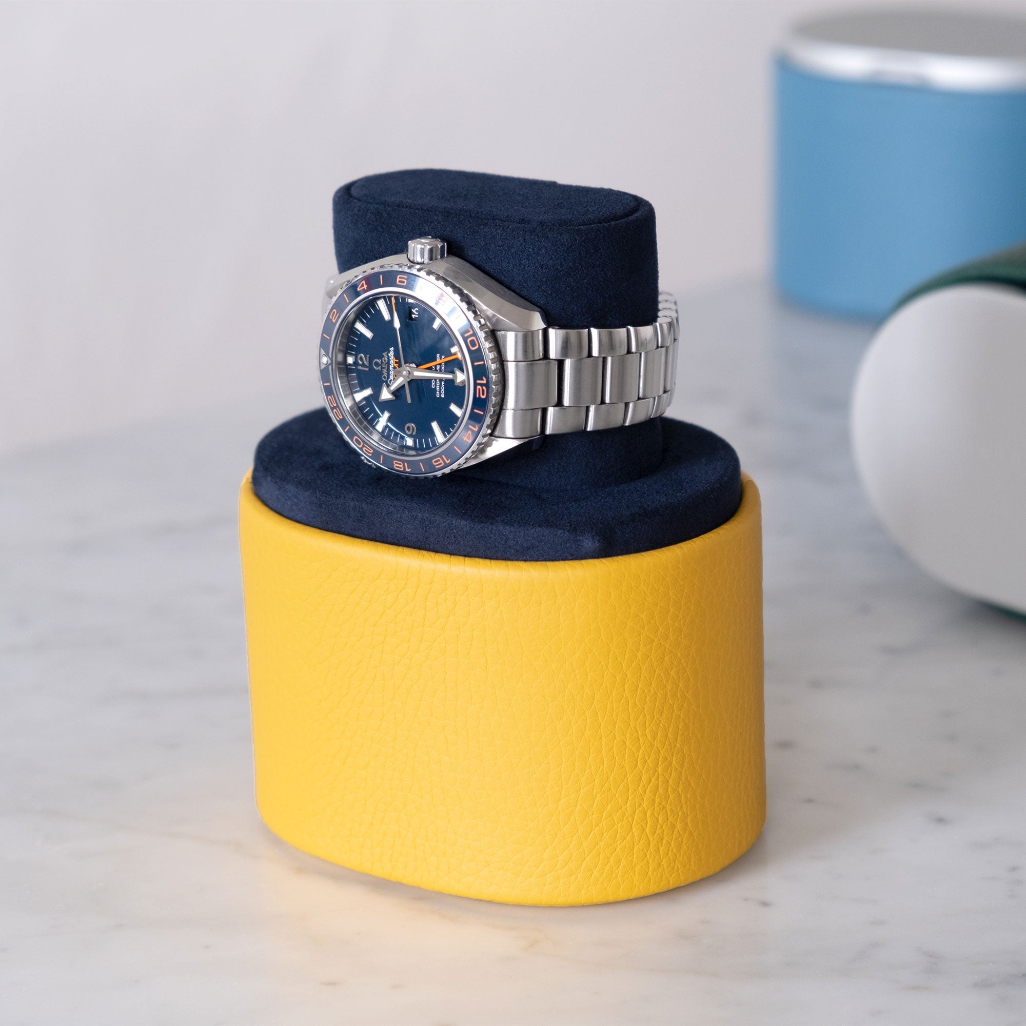 Lifestyle shot of handmade Theo watch roll in sunflower leather and deep blue interior holding Omega Seamaster Planet Ocean 600M Good Planet luxury watch