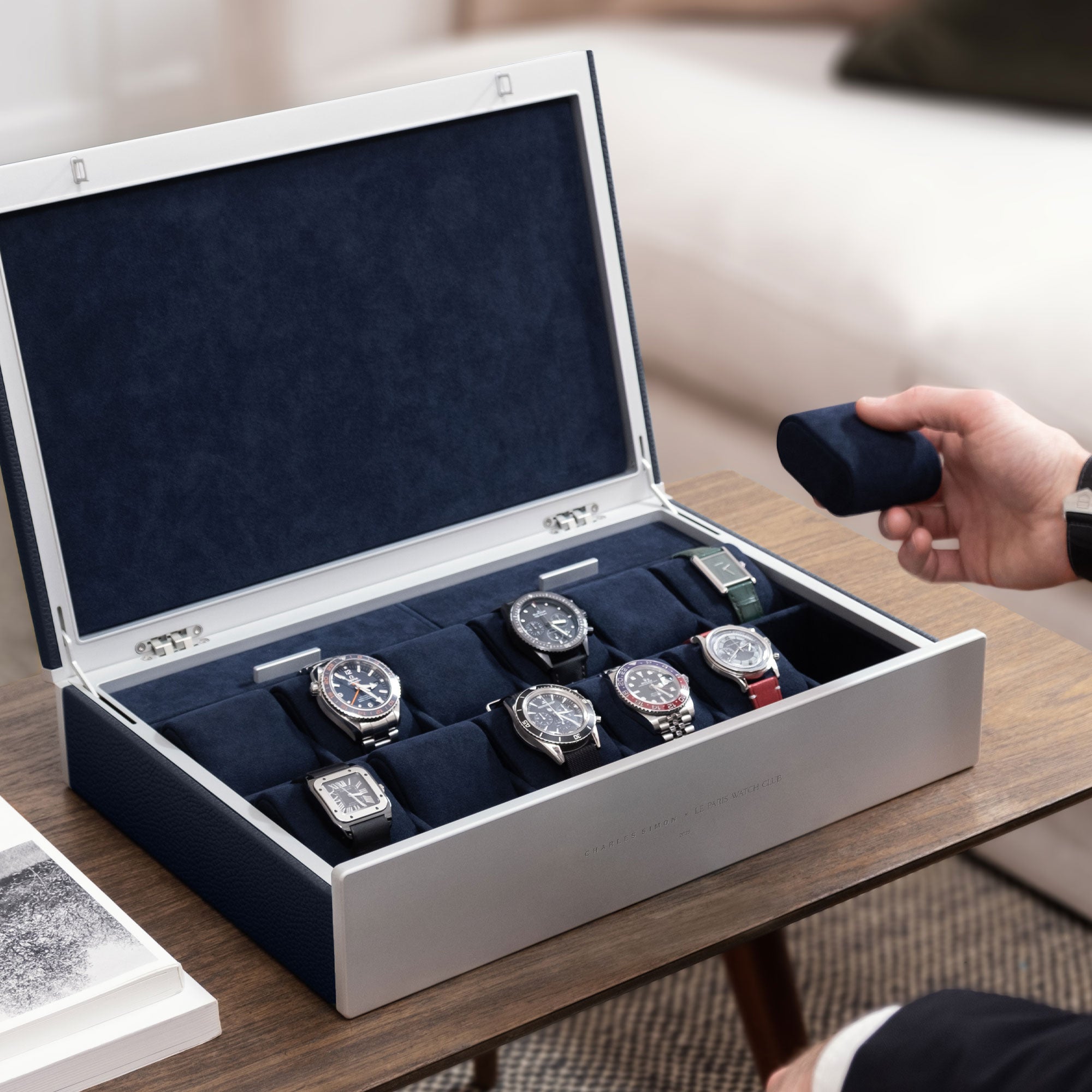 Lifestyle photo of man taking a removable watch cushion in deep blue from his Charles Simon x Paris Watch Club Spence 12 Watch box.