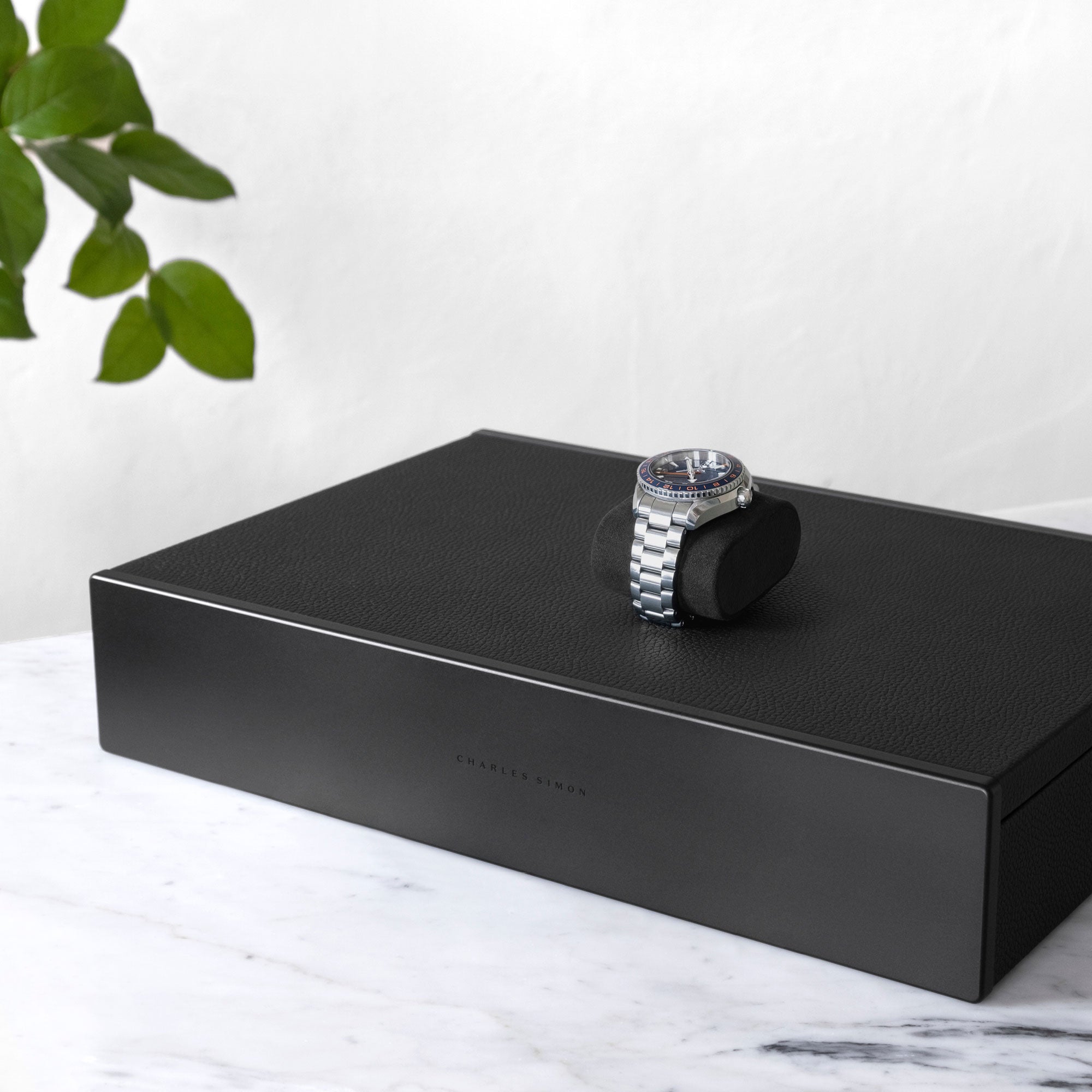 Closed Spence Watch box in black leather and black anodized aluminum and carbon fiber casing with luxury watch displayed on top of it. 