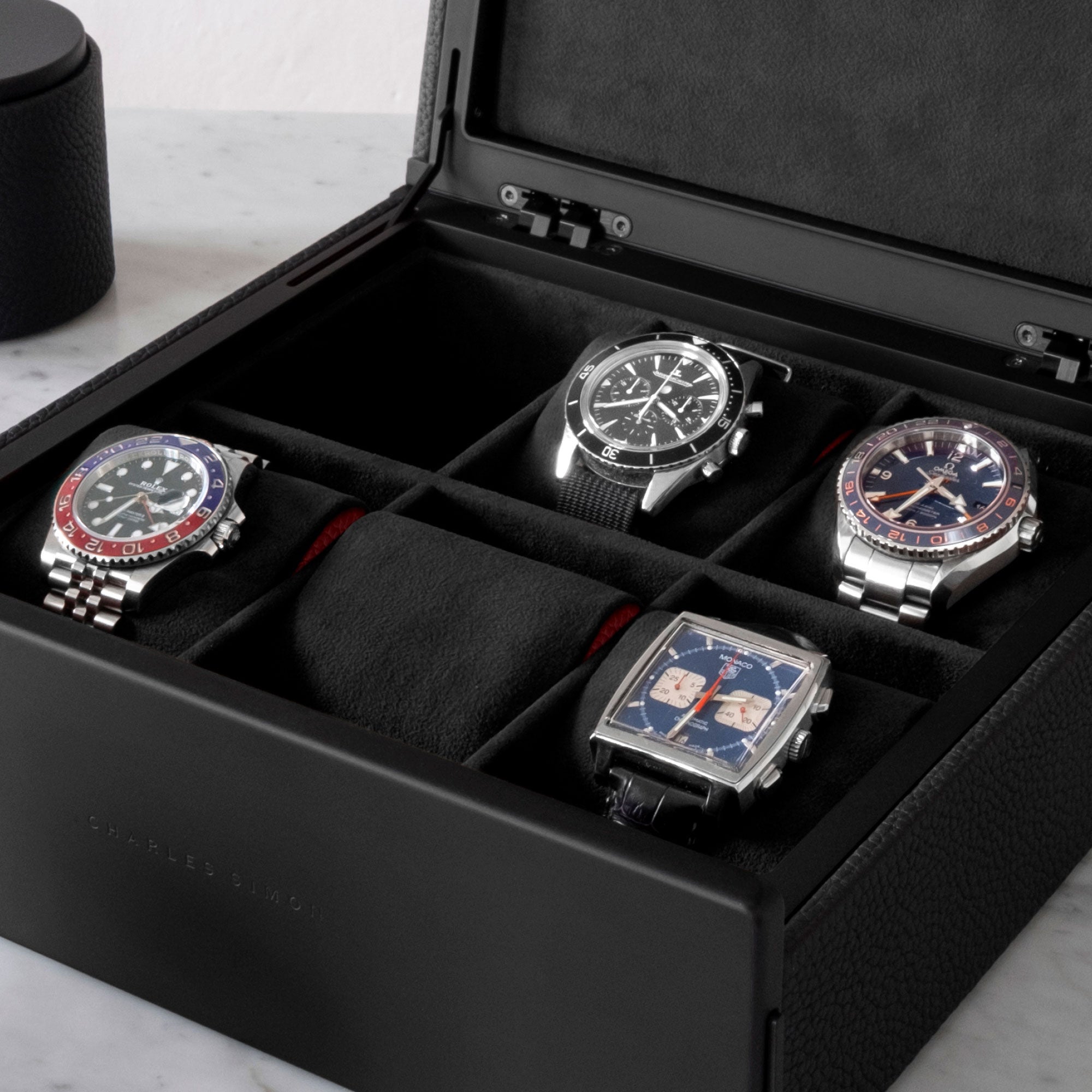 Detail photo of Rolex, Tagheuer, Omega and JaegeLeCoultre watches in all black Spence Watch box with red leather accents