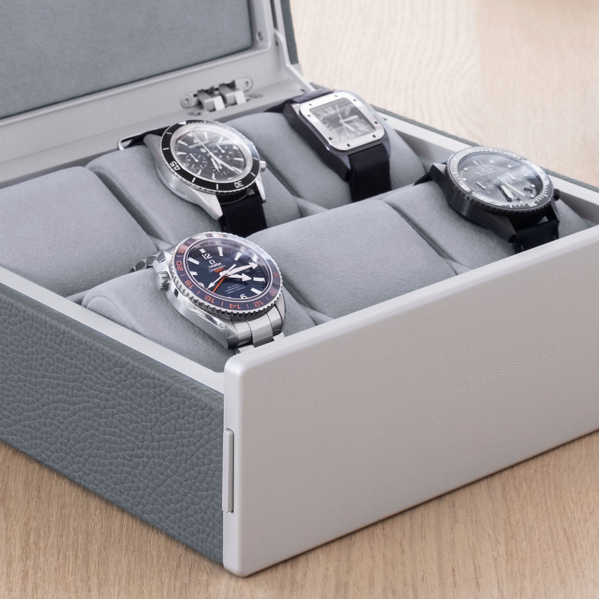 Lifestyle shot of Spence luxury watch box for 6 watches in cloud grey leather filled with men's watches including Blancpain, Omega and Jaeger Lecoultre placed on removable fog grey Alcantara cushions