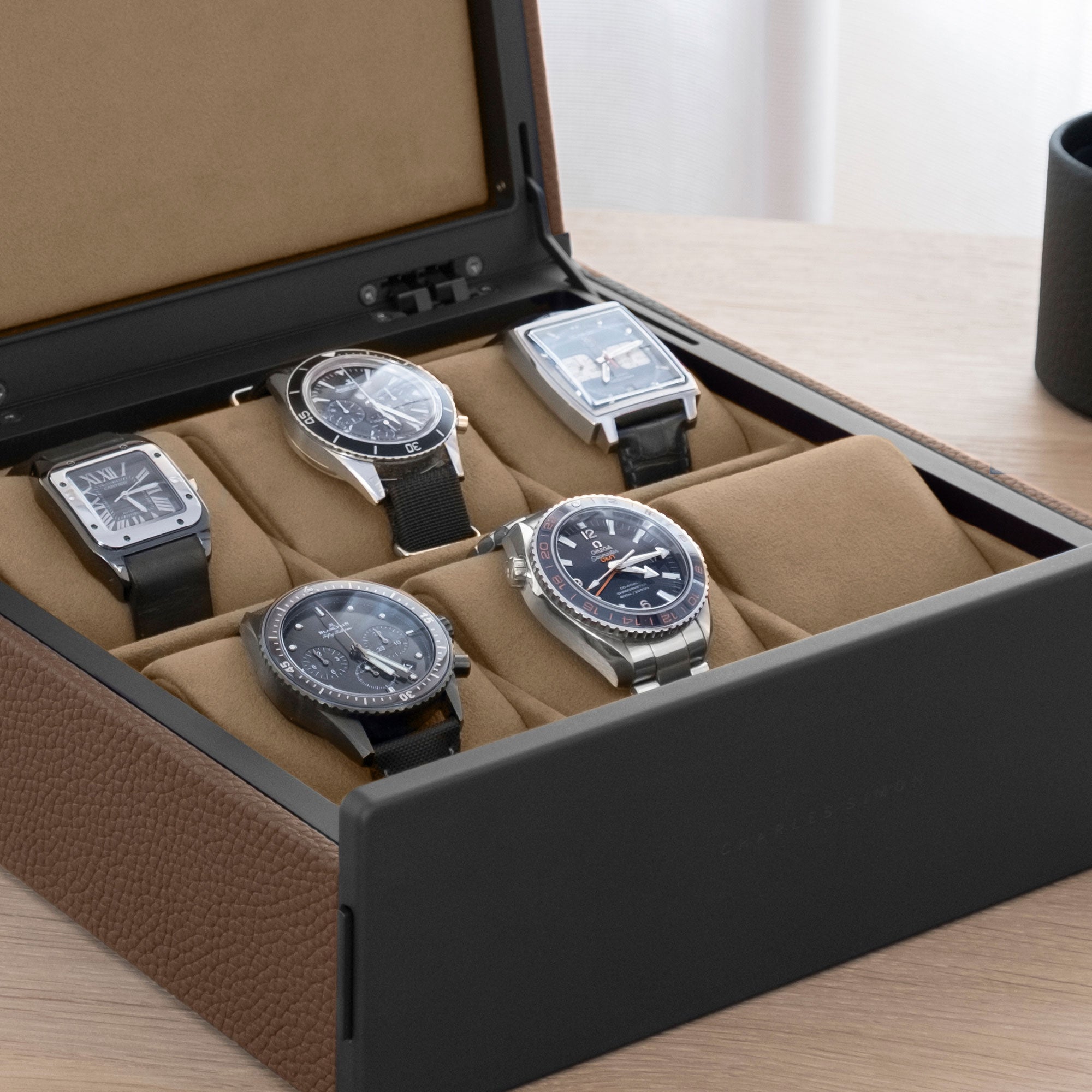 Lifestyle shot of Spence luxury watch box for 6 watches in tan leather filled with men's watches including Jaeger Lecoultre, Omega and Blancpain placed on removable camel Alcantara cushions