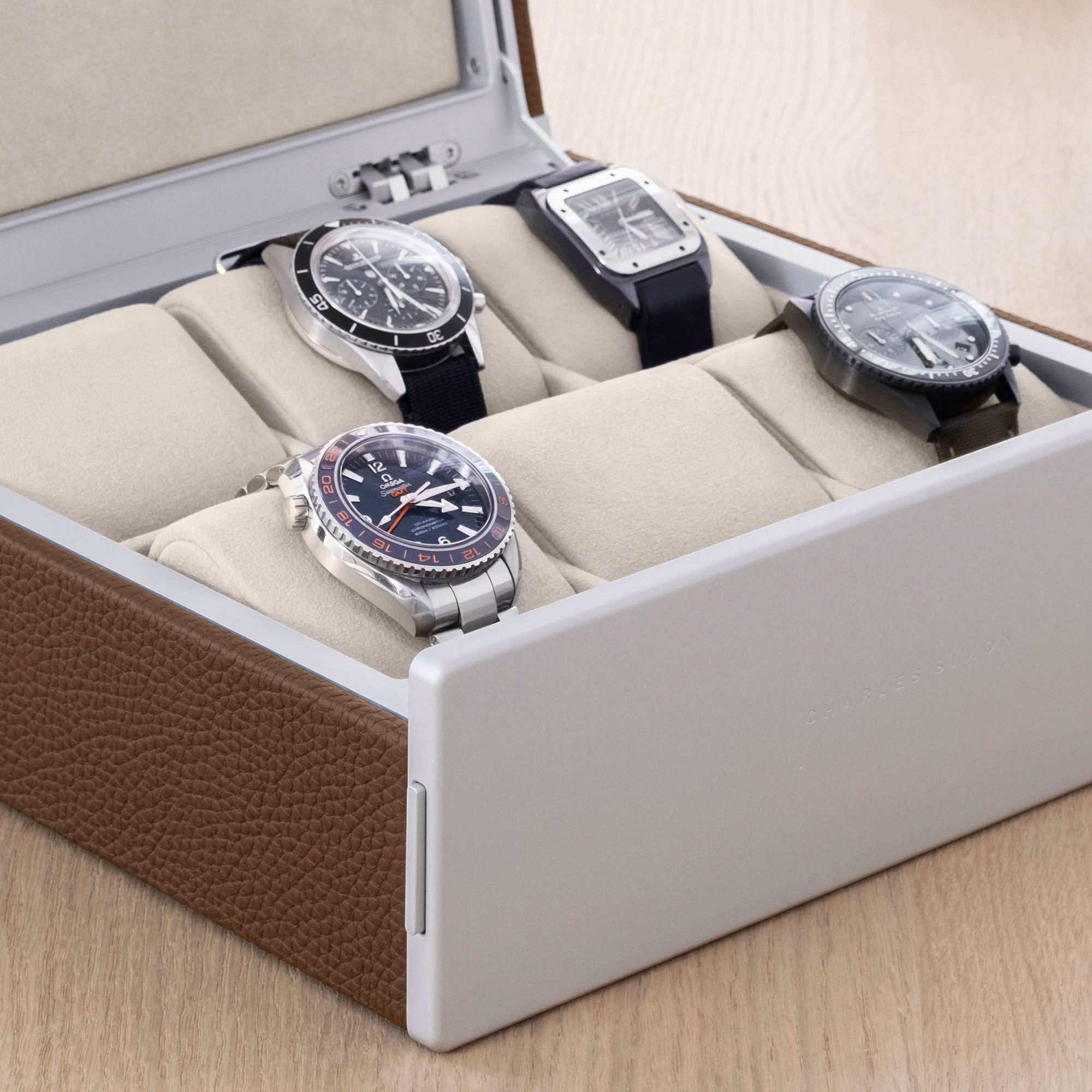 Lifestyle shot of Spence luxury watch box for 6 watches in tan leather filled with men's watches including Blancpain, Omega and Jaeger Lecoultre placed on removable eggshell Alcantara cushions