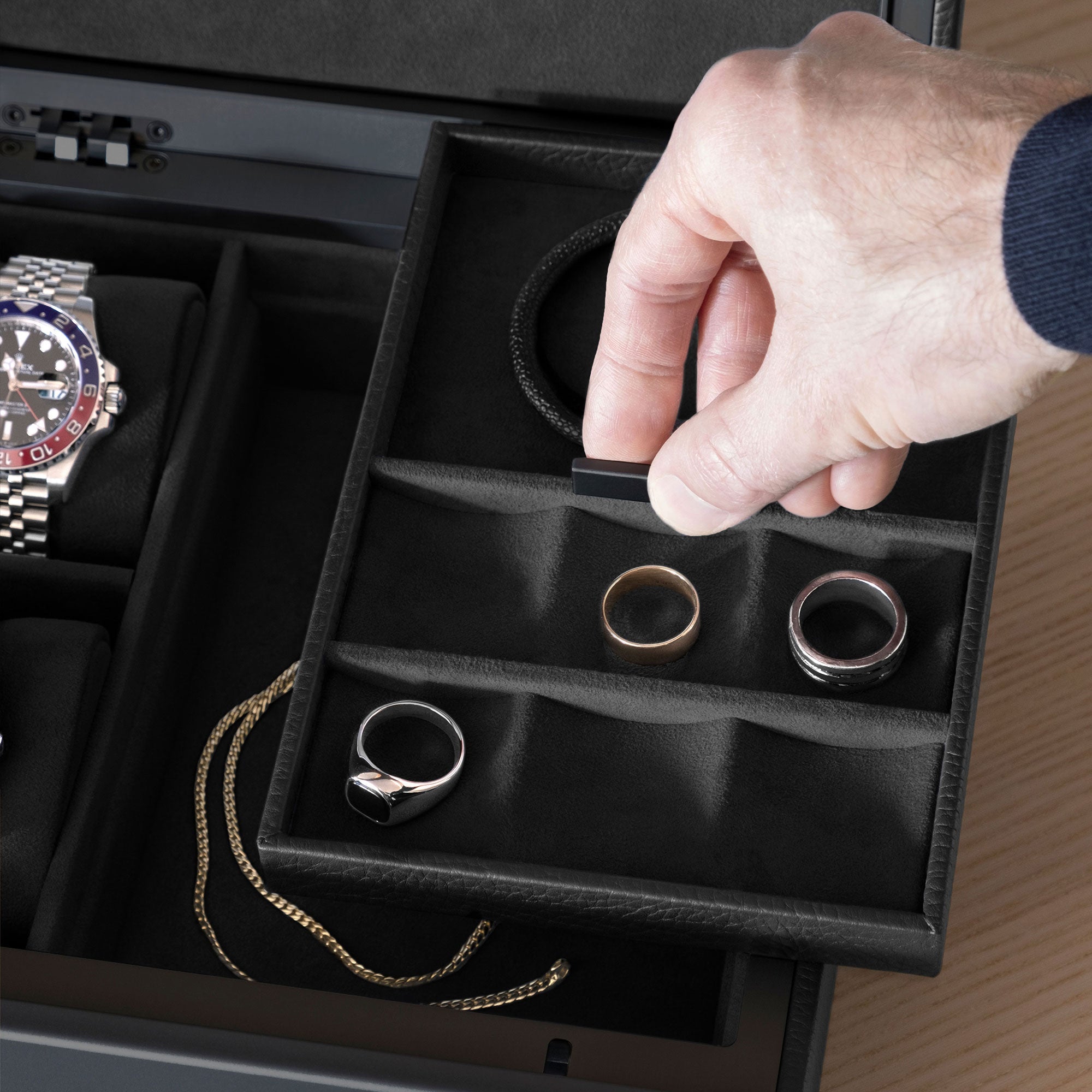 Closeup shot of man grabbing movable jewelry compartment of the all black Taylor 2 Watch and Jewelry box holding silver and gold rings and a black leather bracelet