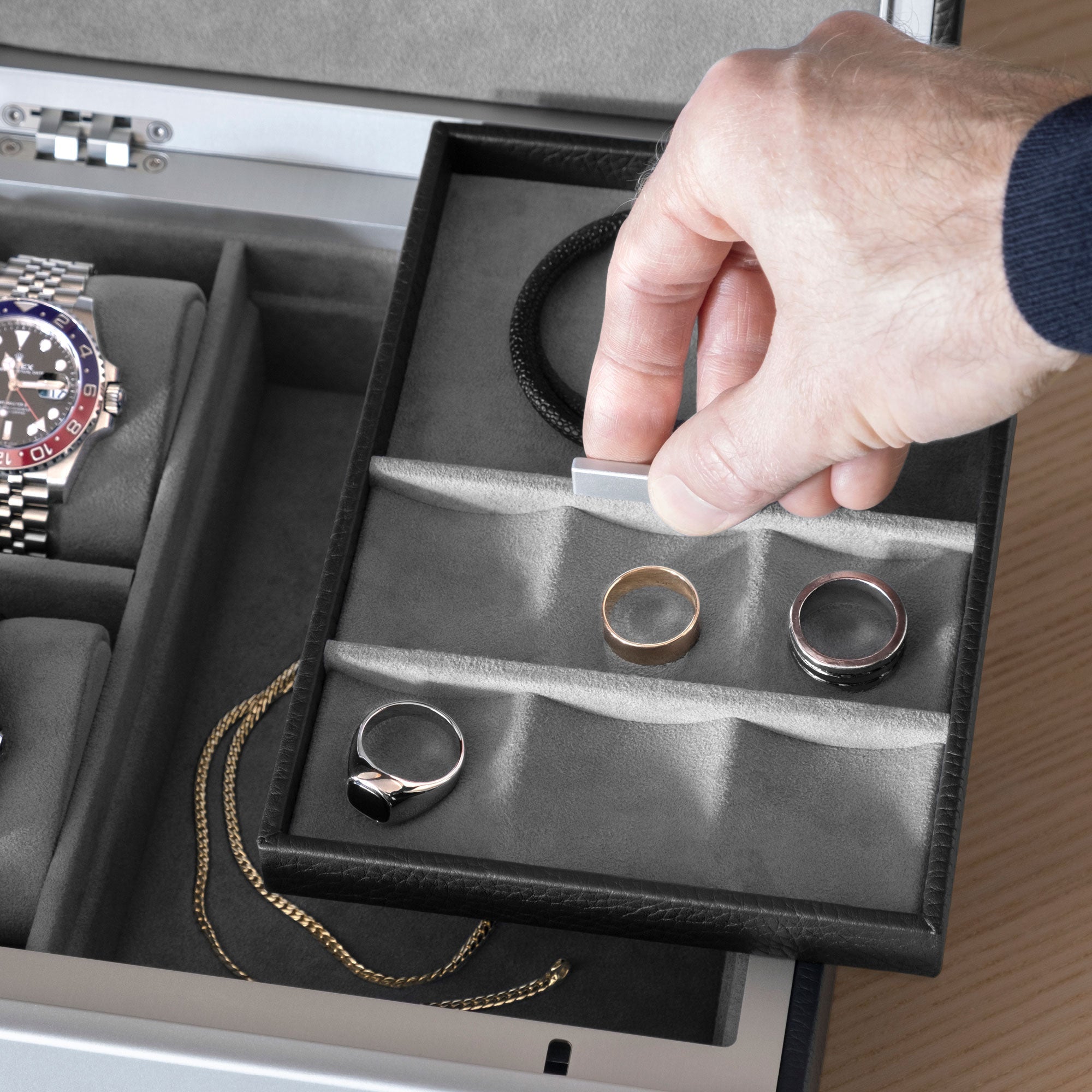Closeup shot of man grabbing movable jewelry compartment of the black leather and fog grey interior Taylor 2 Watch and Jewelry box holding silver and gold rings and a black leather bracelet