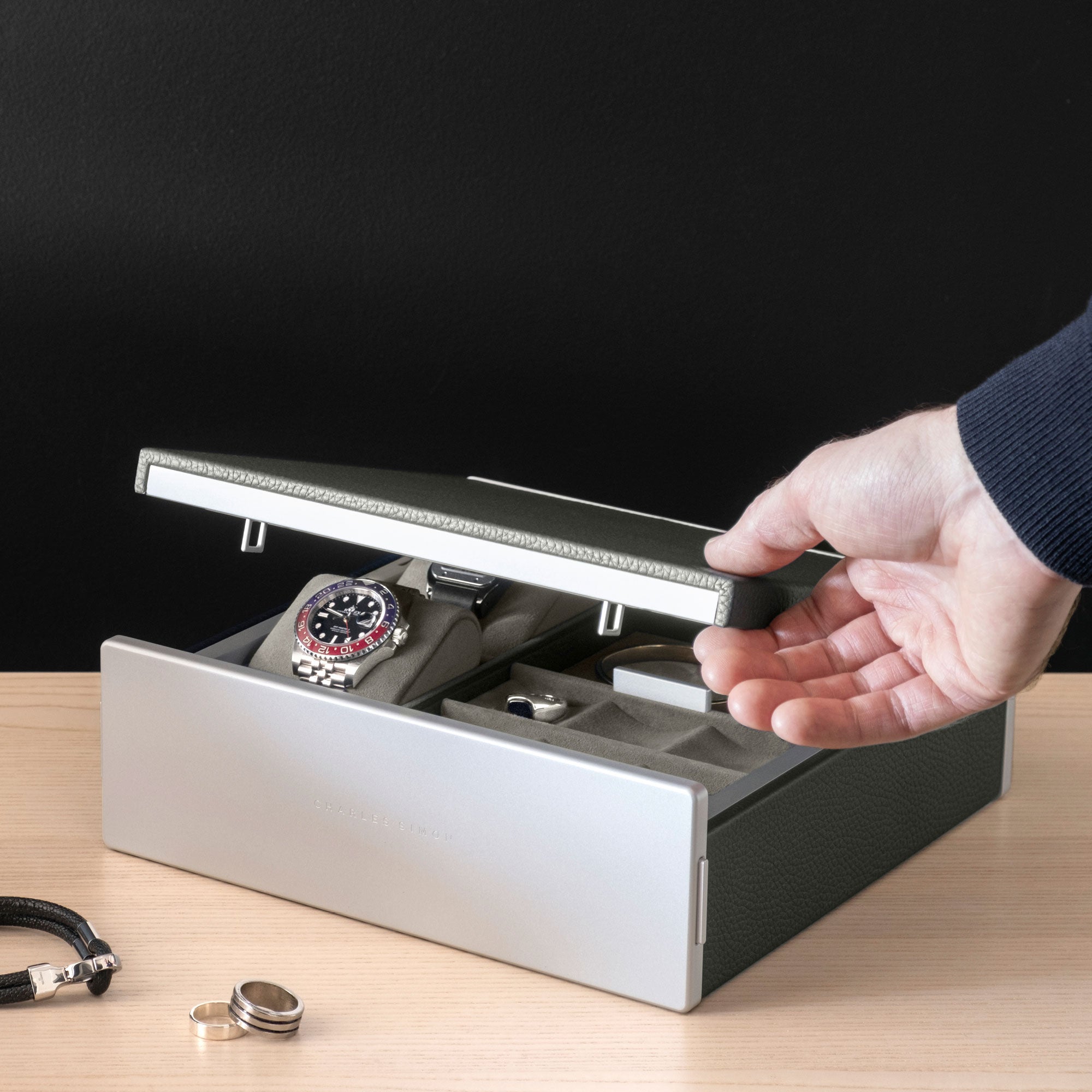 Man opening lid of the Taylor 2 Watch and Jewelry box in graphite leather and sea sand interior. The watch box and jewelry box is holding a Rolex on a watch cushion as well as silver jewelry