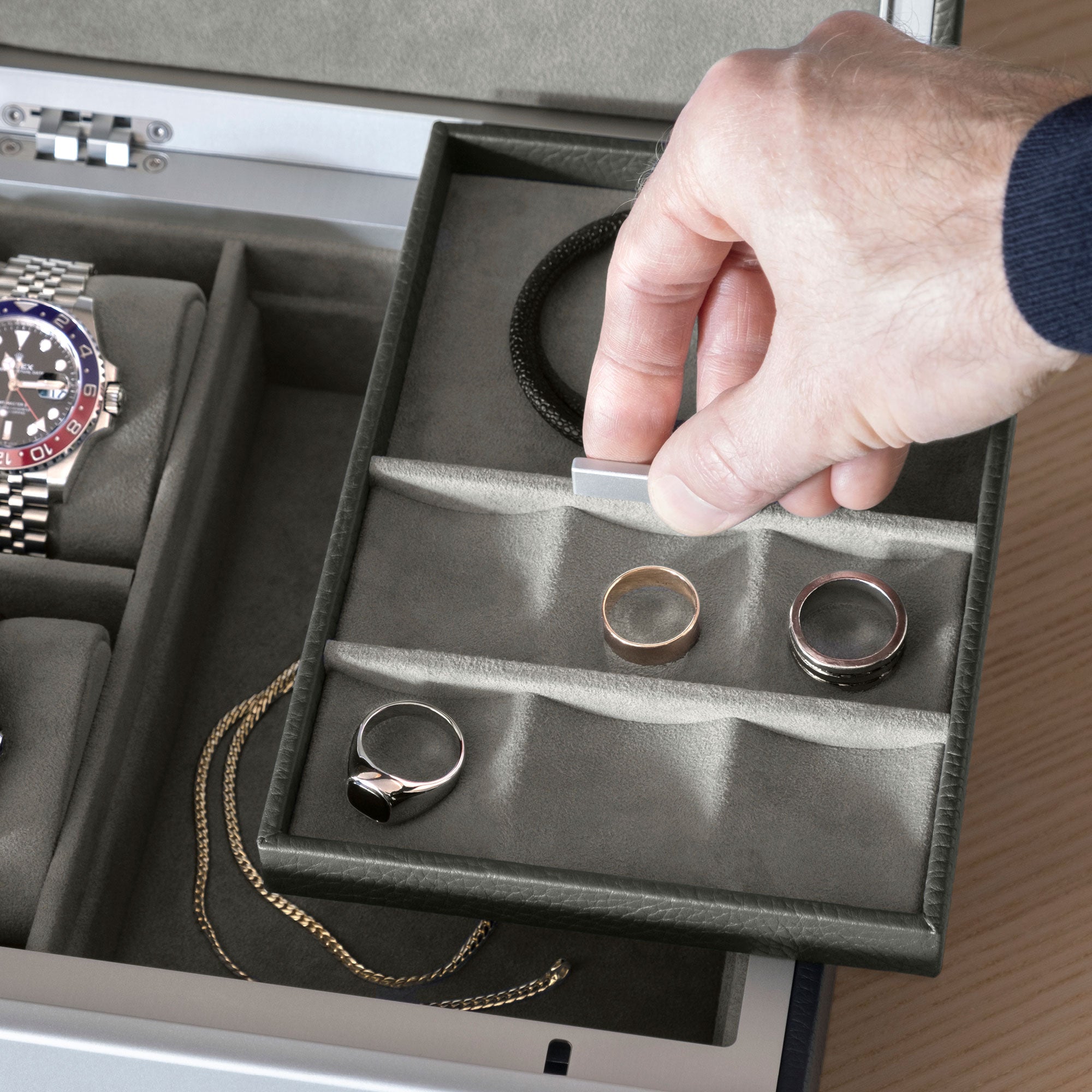 Detail shot of man lifting up jewelry tray holding rings and bracelets. Necklace is placed in bottom storage compartment of the Taylor 2 Watch and Jewelry box and two watches are displayed on sea sand watch cushions on the side. 