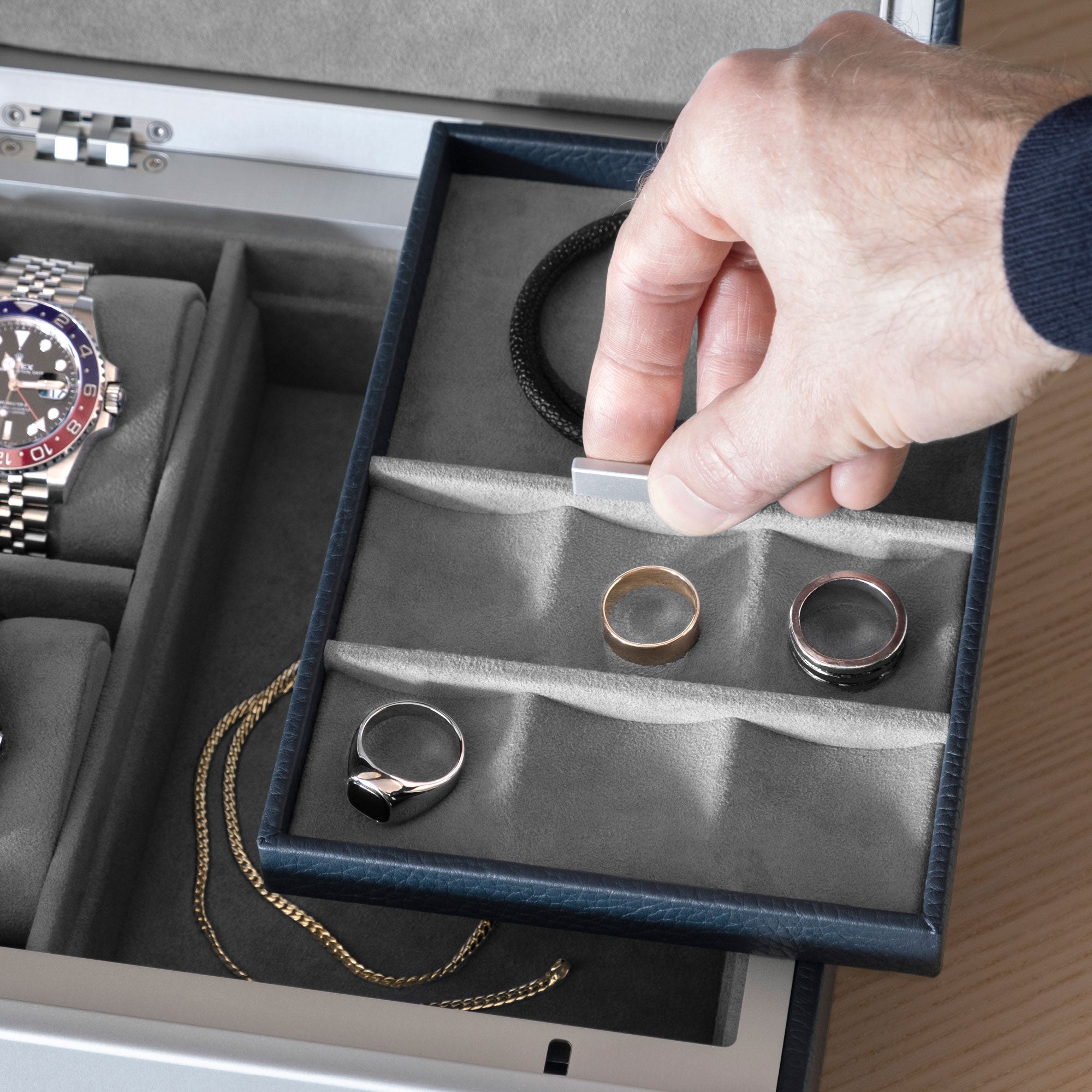 Closeup shot of man grabbing movable jewelry compartment of the marine leather and fog grey interior Taylor 2 Watch and Jewelry box holding silver and gold rings and a black leather bracelet
