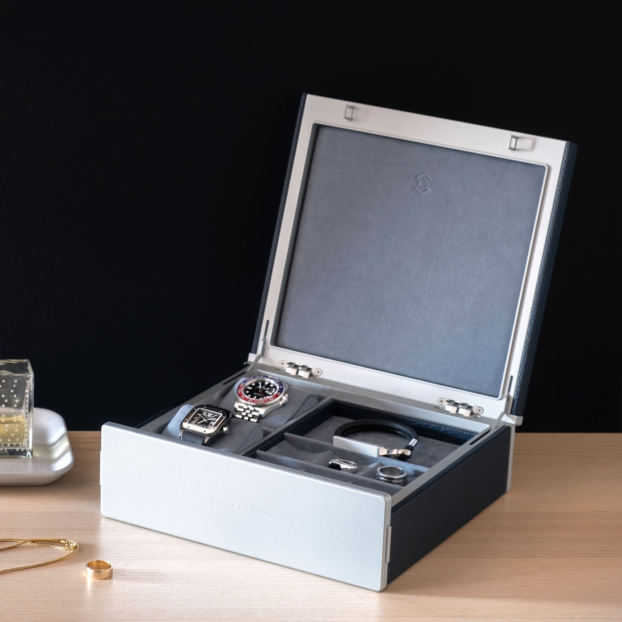 Lifestyle photo of open Taylor 2 Watch and Jewelry box displaying a collection of silver and gold jewelry in its convenient compartments and holding two luxury watches on removable watch cushions