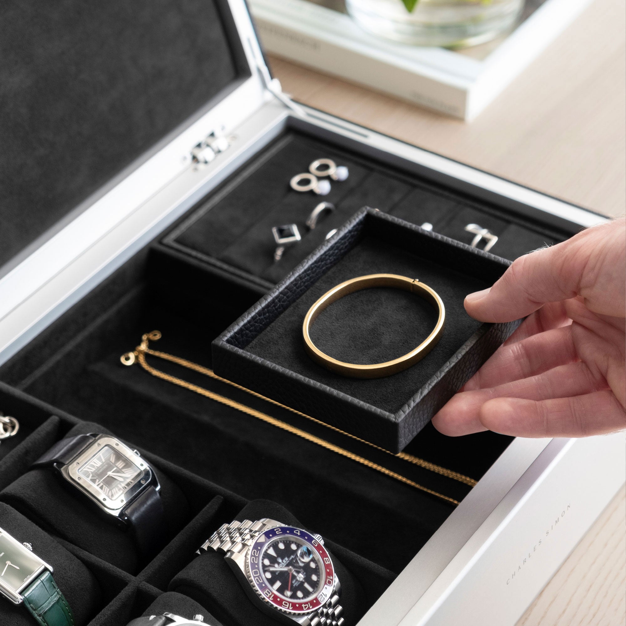 Detail photo of man holding mobile jewelry tray containing a gold bracelet from the black leather and notte interior Taylor 4 Watch and Jewelry box. The Taylor 4 Watch and Jewelry box is storing 4 luxury watches and a collection of fine jewelry, including silver rings, earrings, bracelets and necklaces.