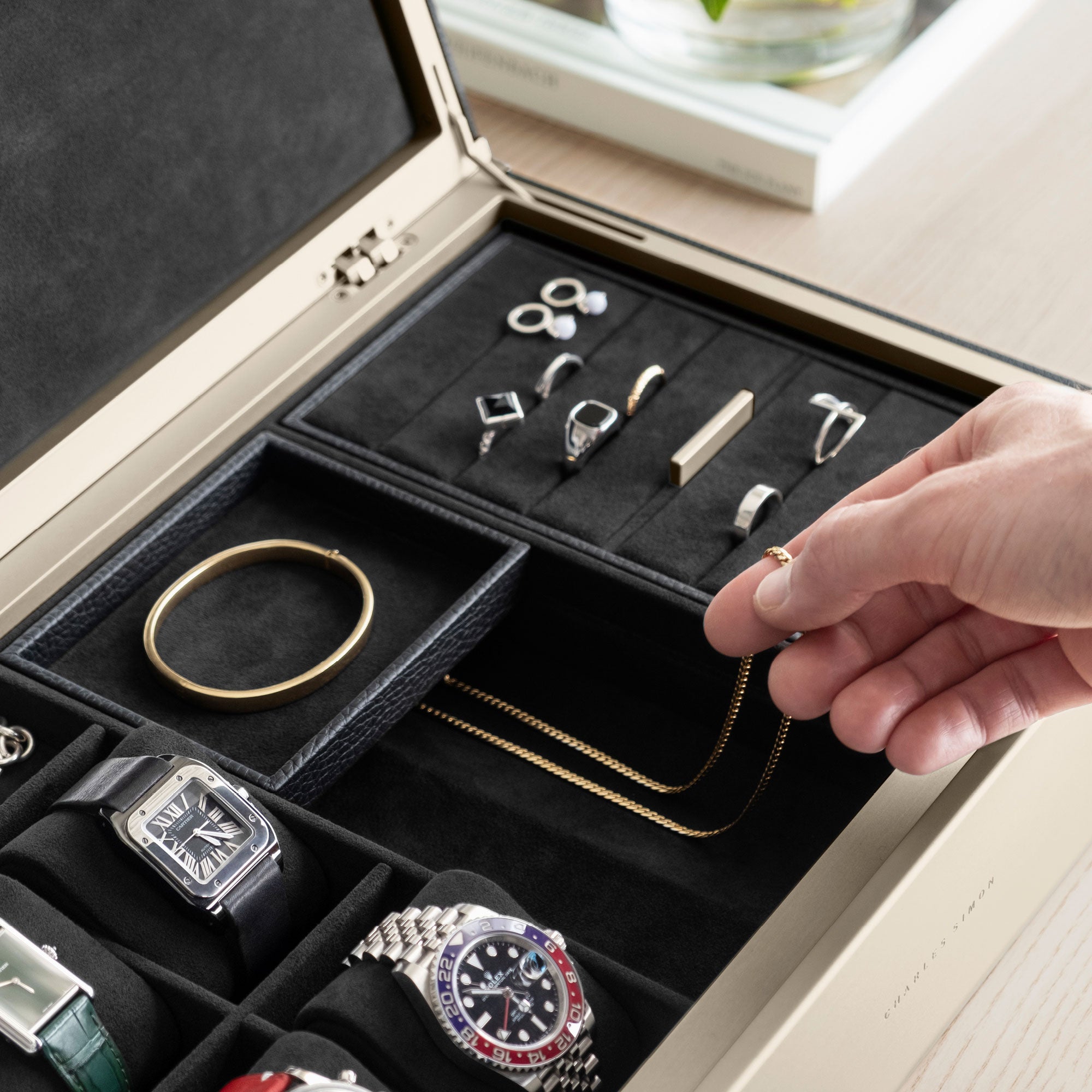 Detail photo of man taking gold necklace from the organization compartment of his gold Taylor 4 Watch and jewelry box in black leather.