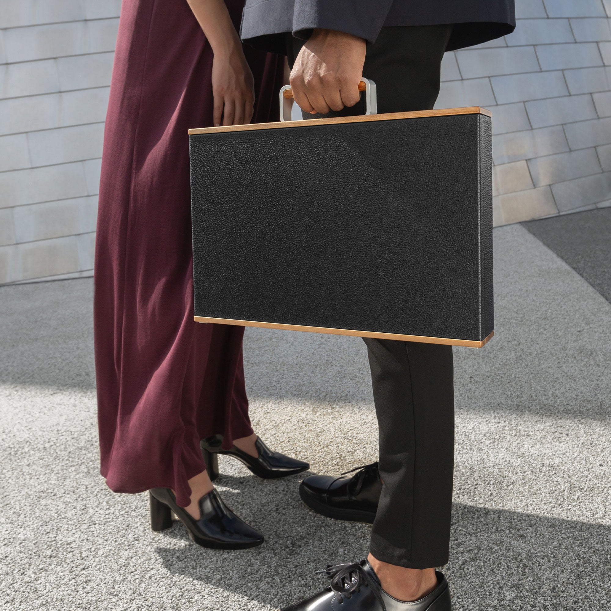 Man and woman standing together, holding the minimalist Mackenzie Briefcase in black leather with wooden details  made from recycled, sustainable timber. 