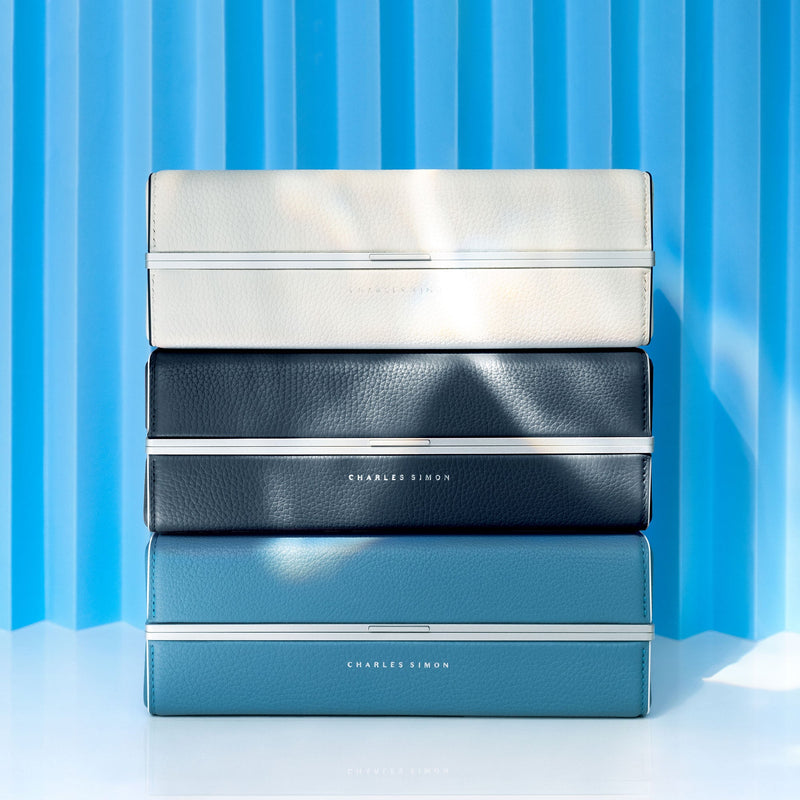Lifestyle shot of three stacked limited edition Moraine toiletry bags in white, marine and sky blue. 