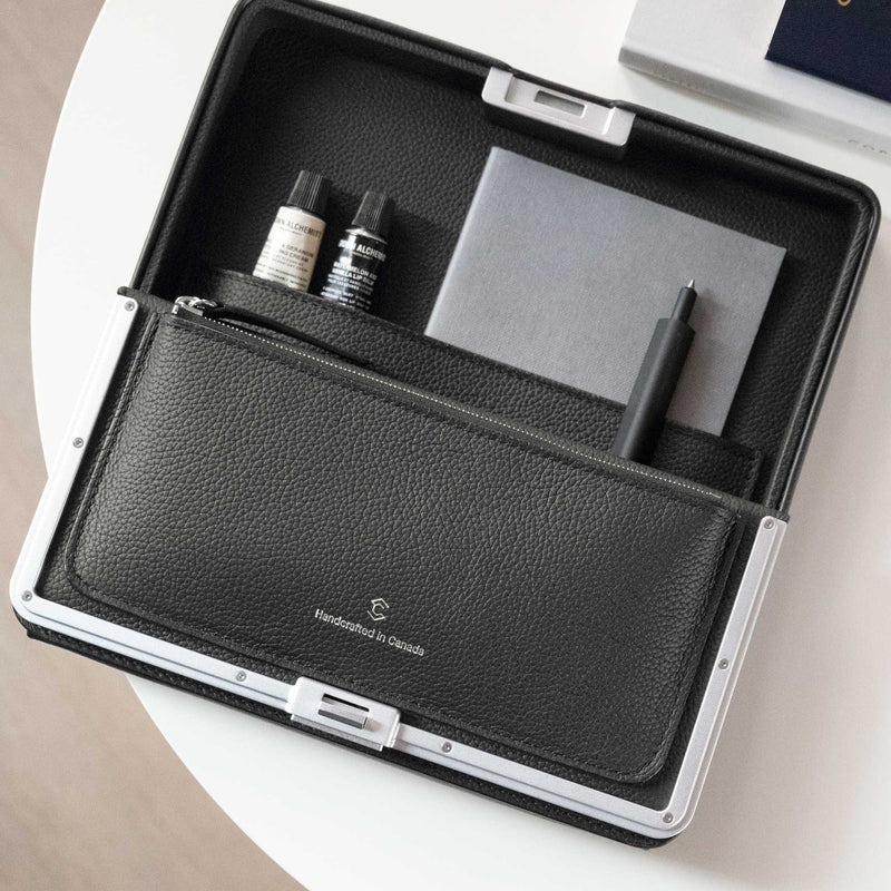 Lifestyle shot of open leather travel wallet in graphite. The wallet contains all travel essentials, including a pen, notebook, hand cream and cosmetics 