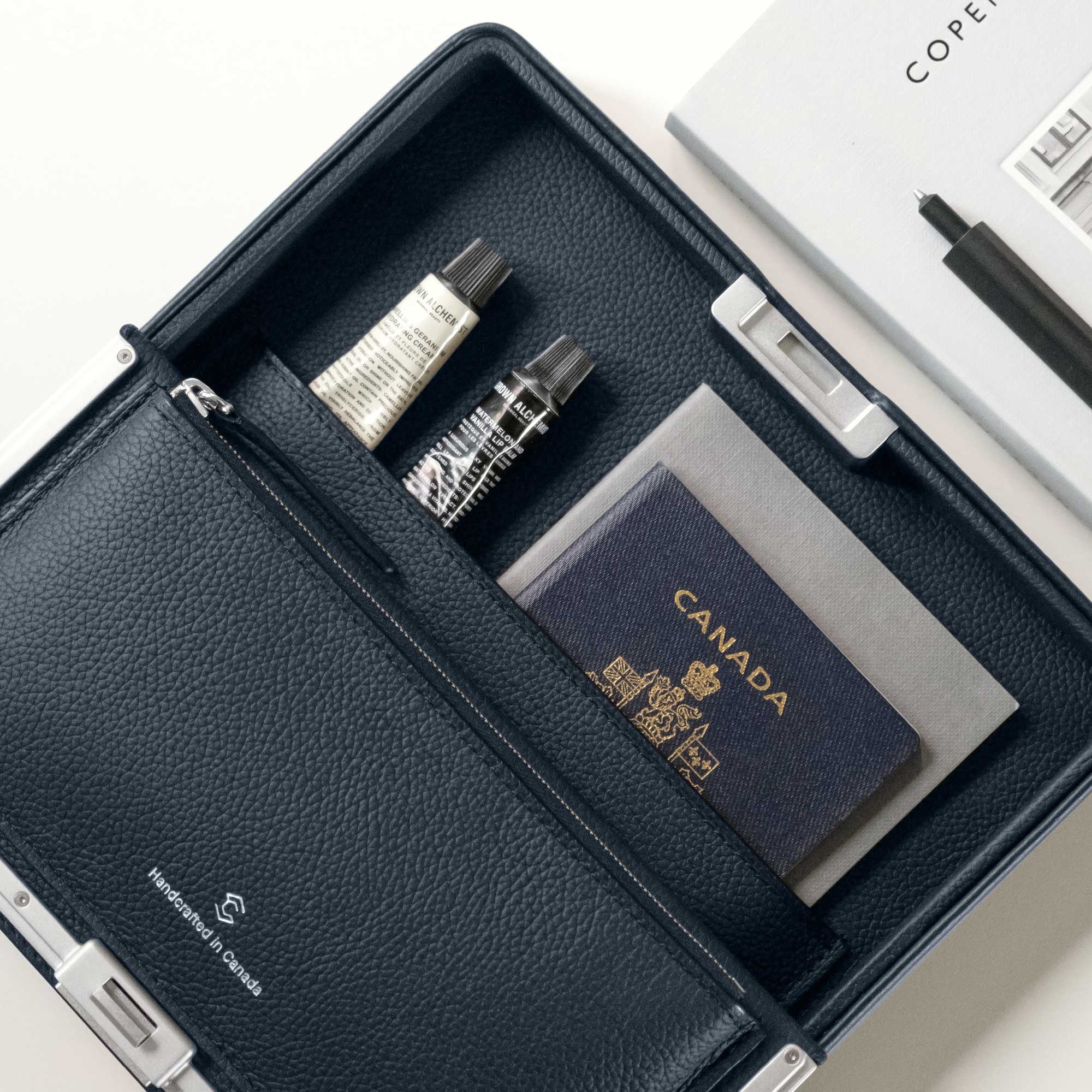 Lifestyle photo showing the elegant Fraser Travel wallet in marine holding a passport, creams, and other travel essentials